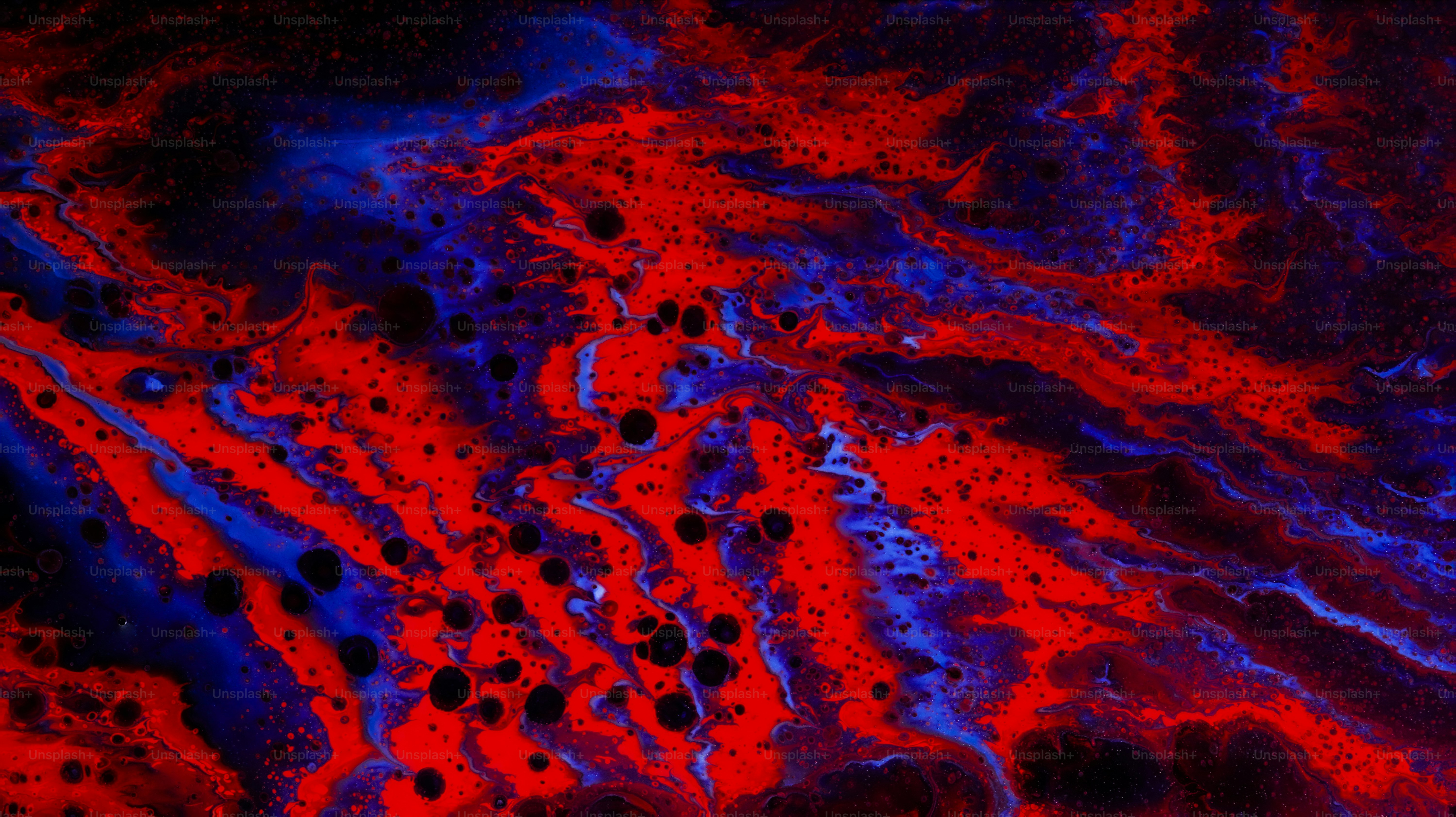 Swirling patterns of vibrant red and deep blue liquid with scattered black spots