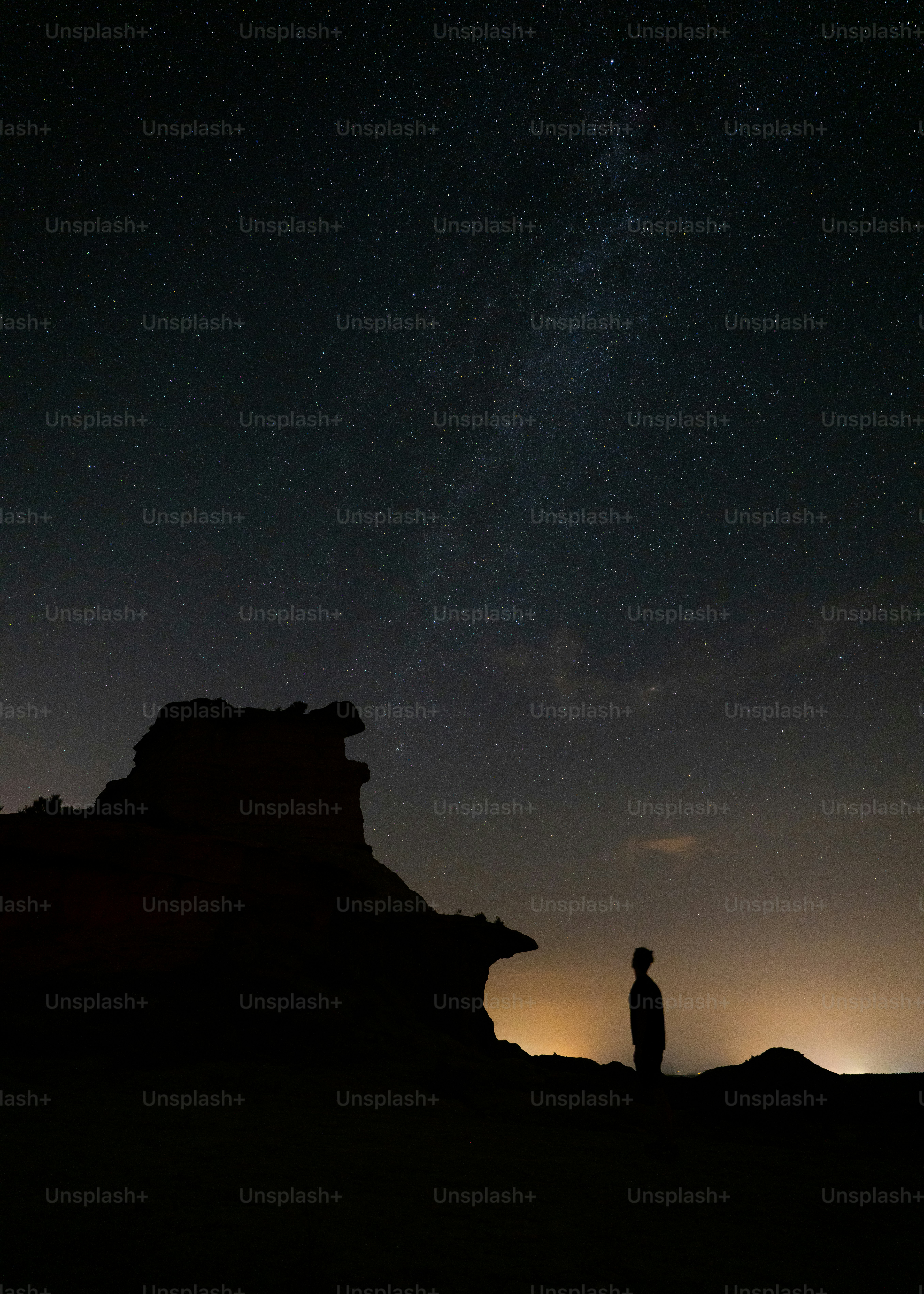 A person in silhouette against a starry night sky and a rocky outcrop