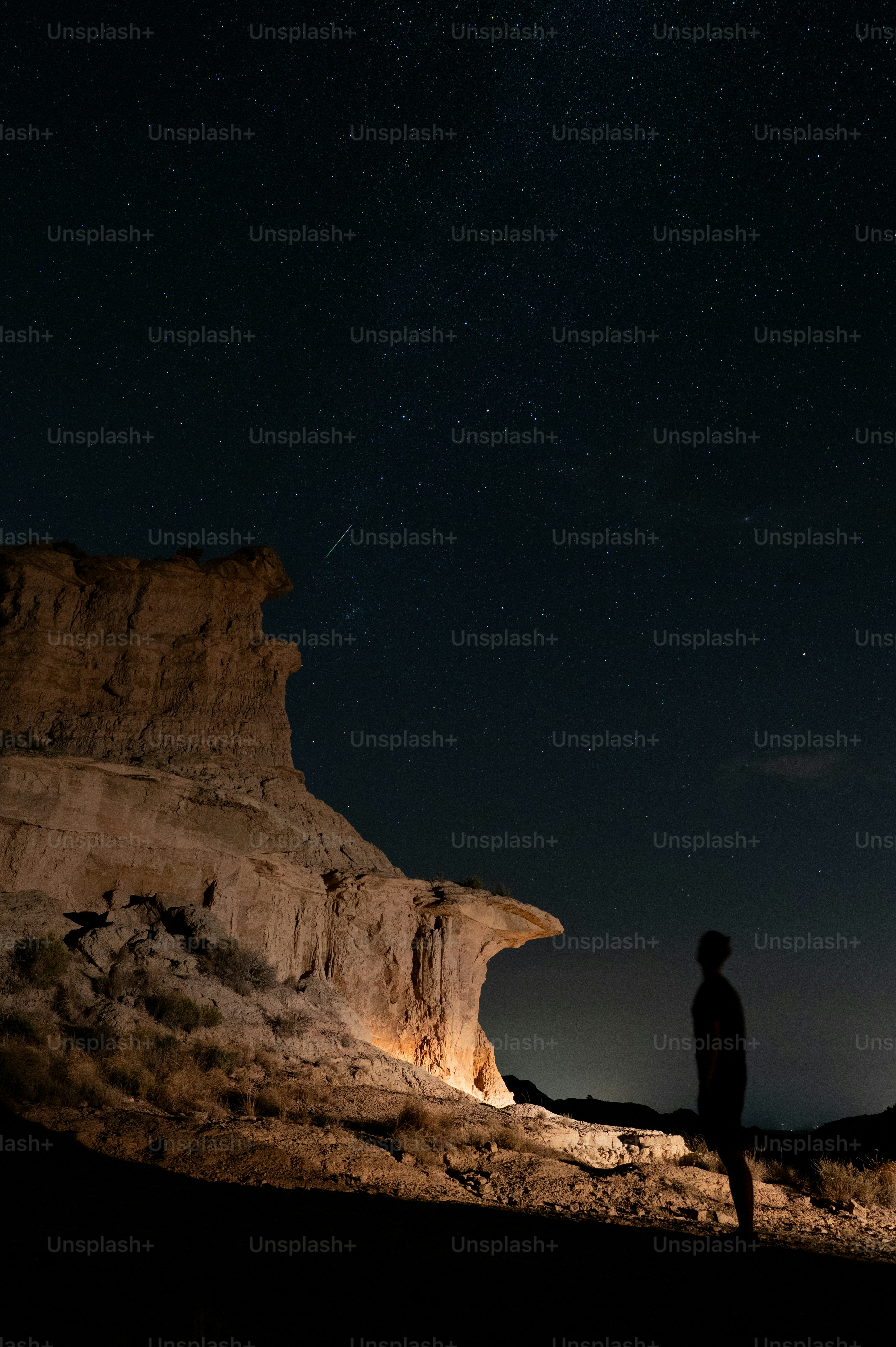 A person in silhouette against a starry night sky beside a rocky cliff