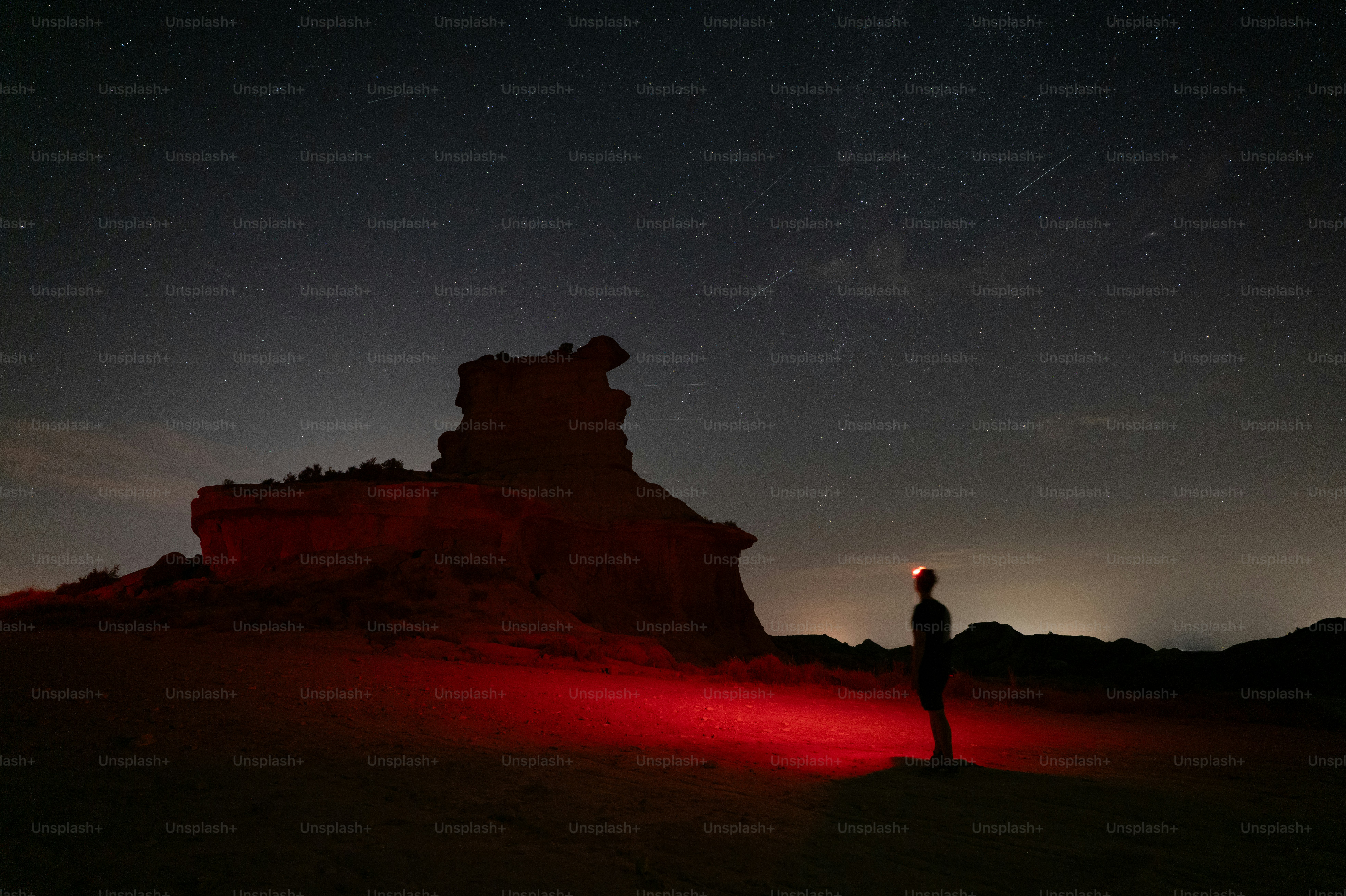 A person with a red headlamp in a dark desert landscape under starry skies