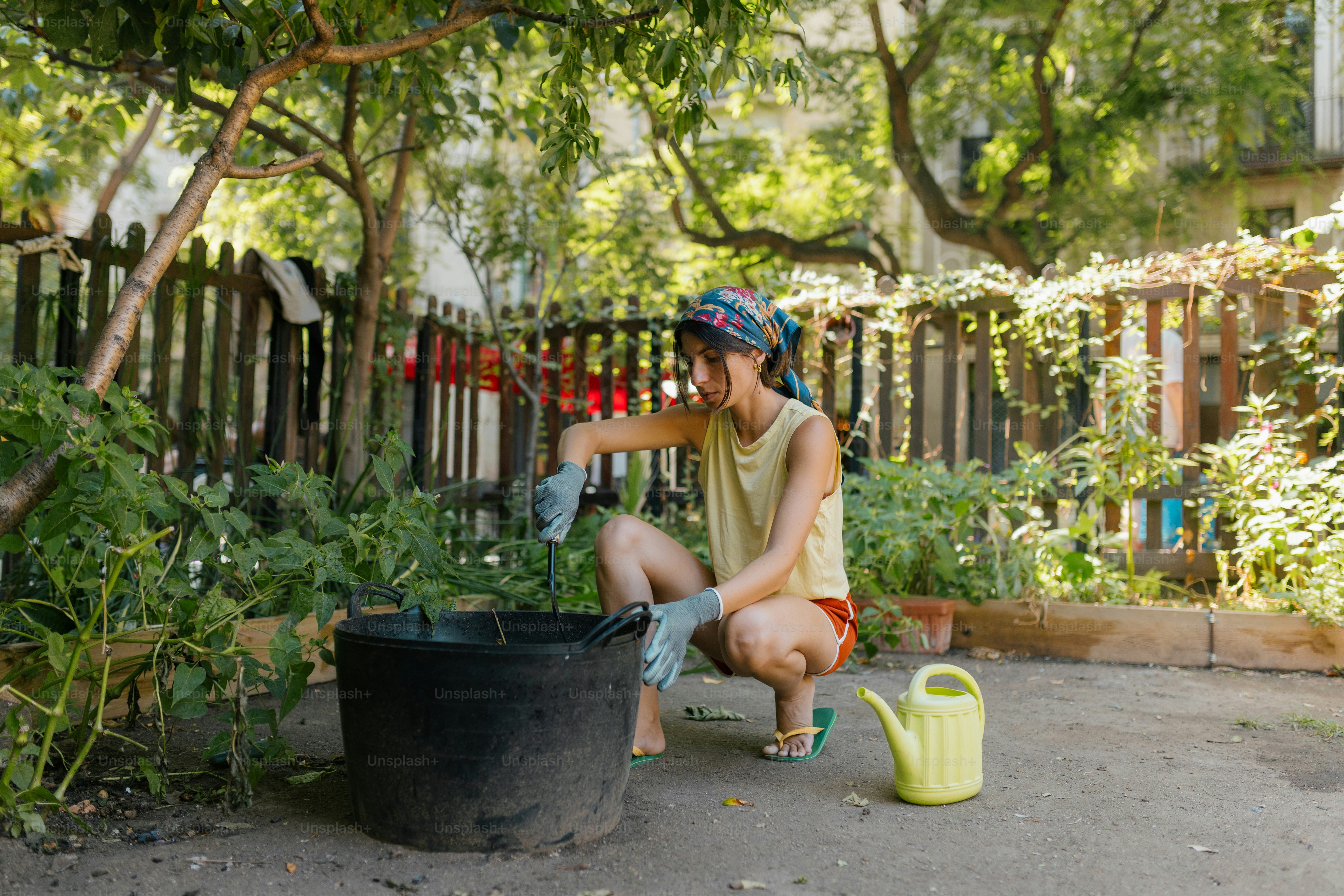 A woman in a headscarf gardening with a black bucket and yellow watering can