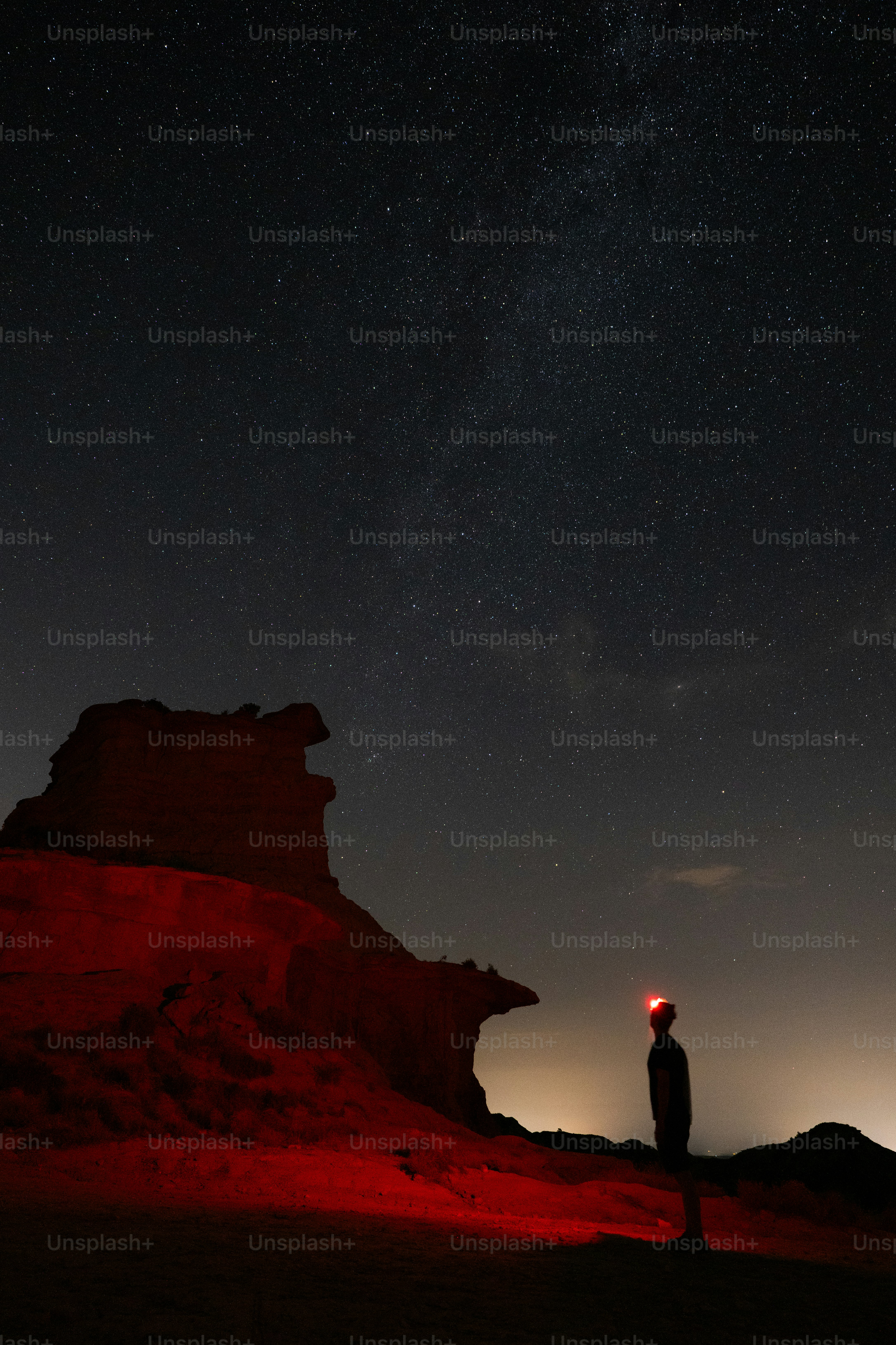 A person with a red headlamp on a rocky outcrop under a starry sky