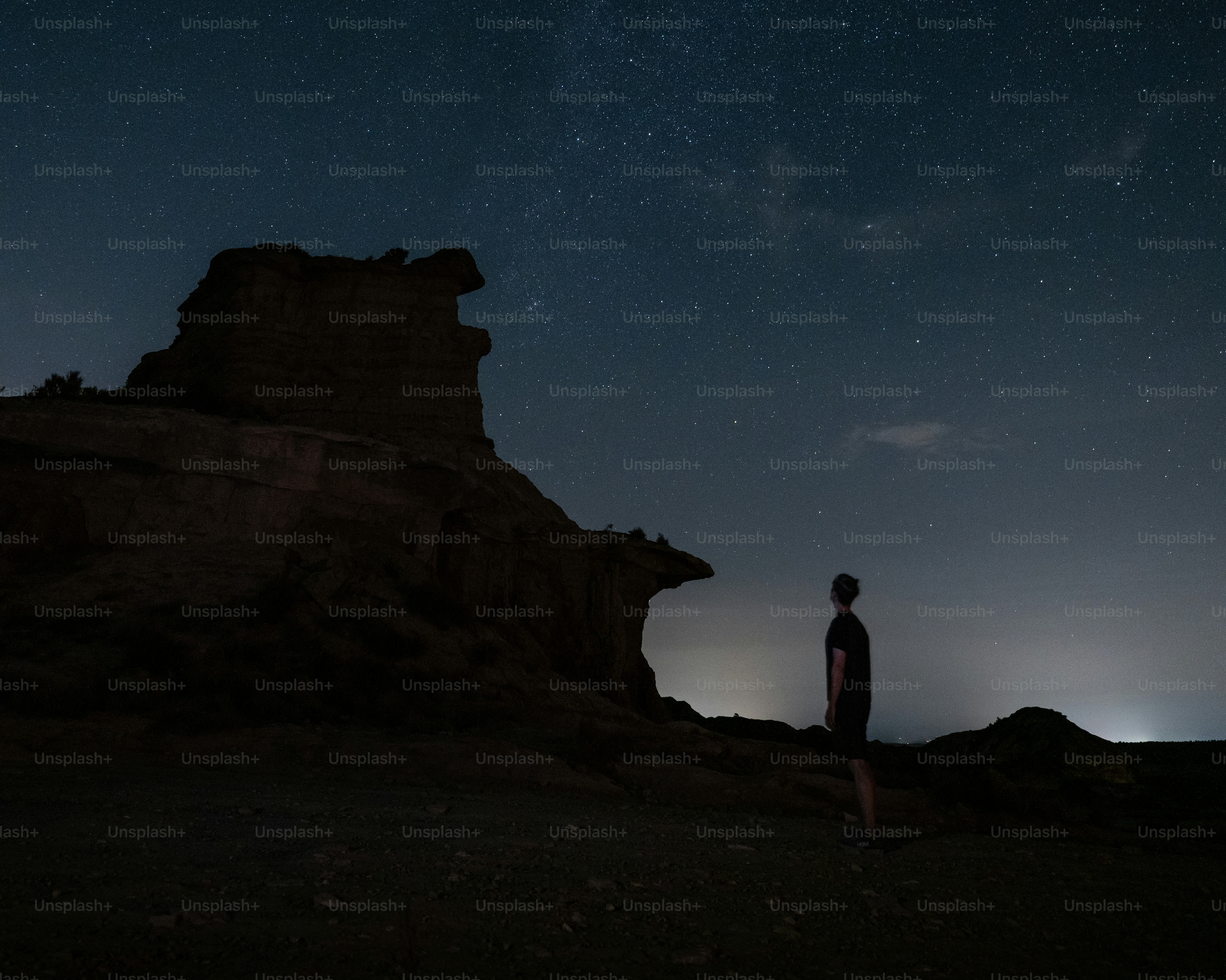 A person in silhouette looking at a starry night sky near a rocky cliff