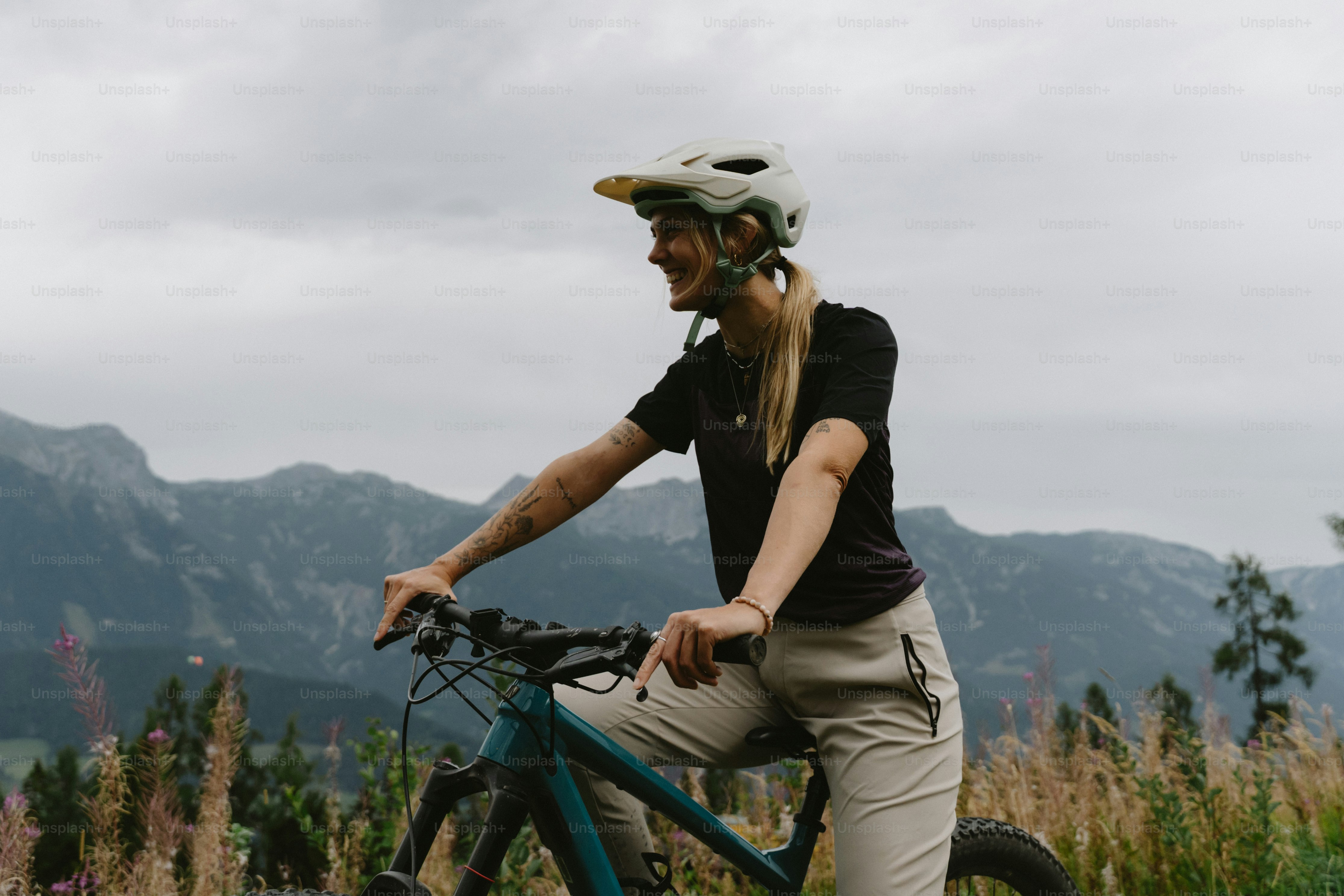 A woman in a helmet cycling on a mountain trail with distant peaks