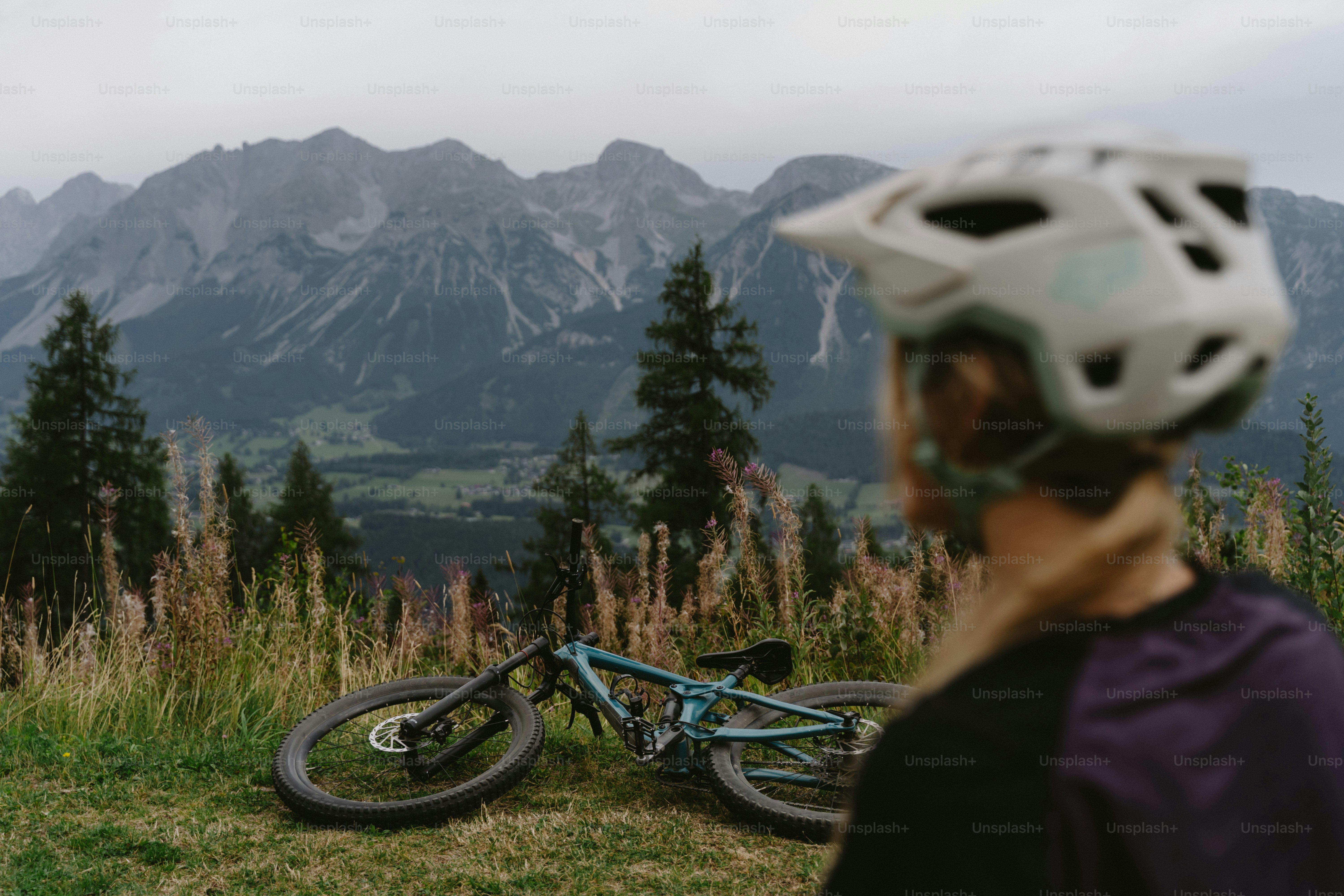 A person in a helmet looking at a mountain bike on a grassy hillside