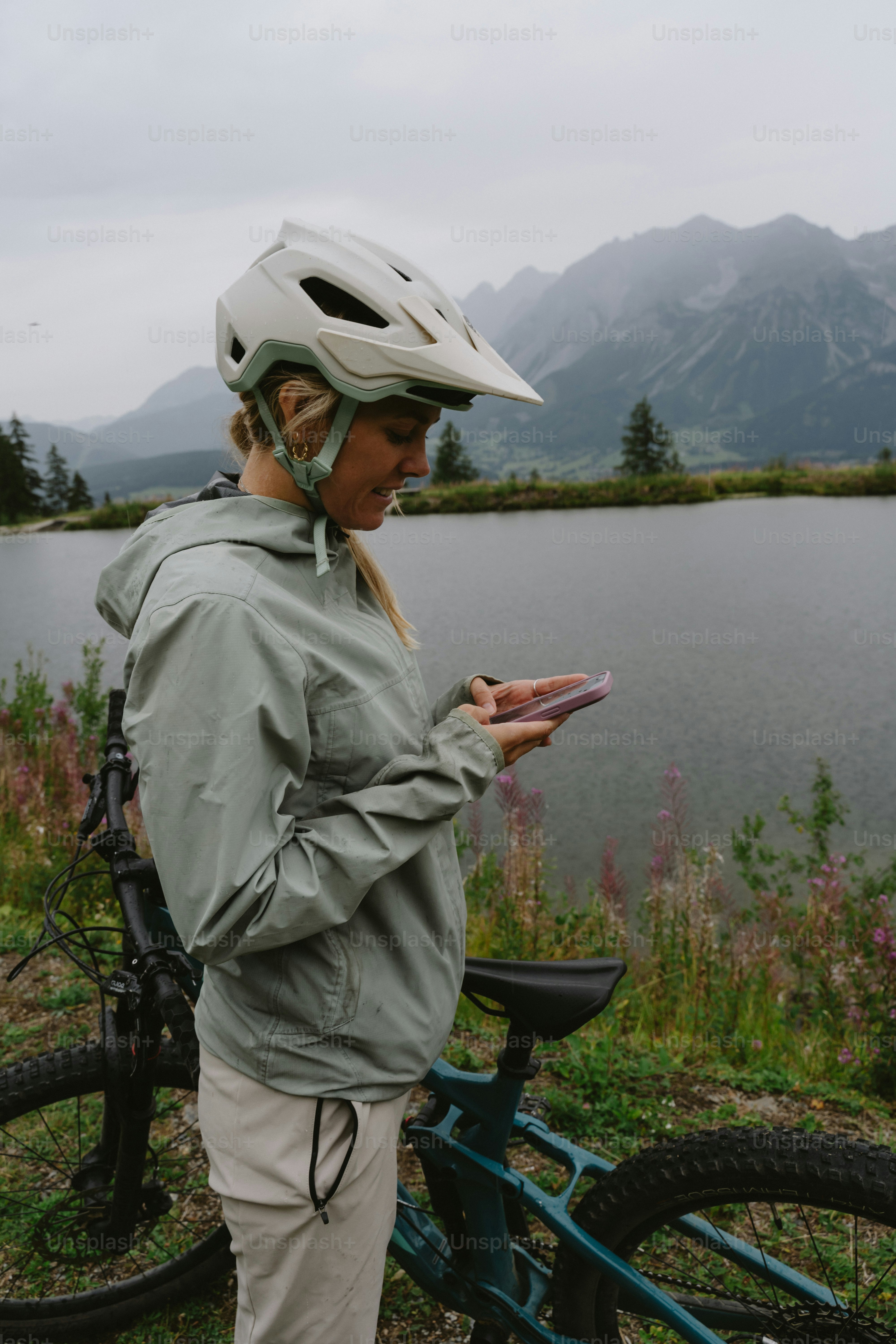 A woman in a cycling helmet using a smartphone beside a mountain lake