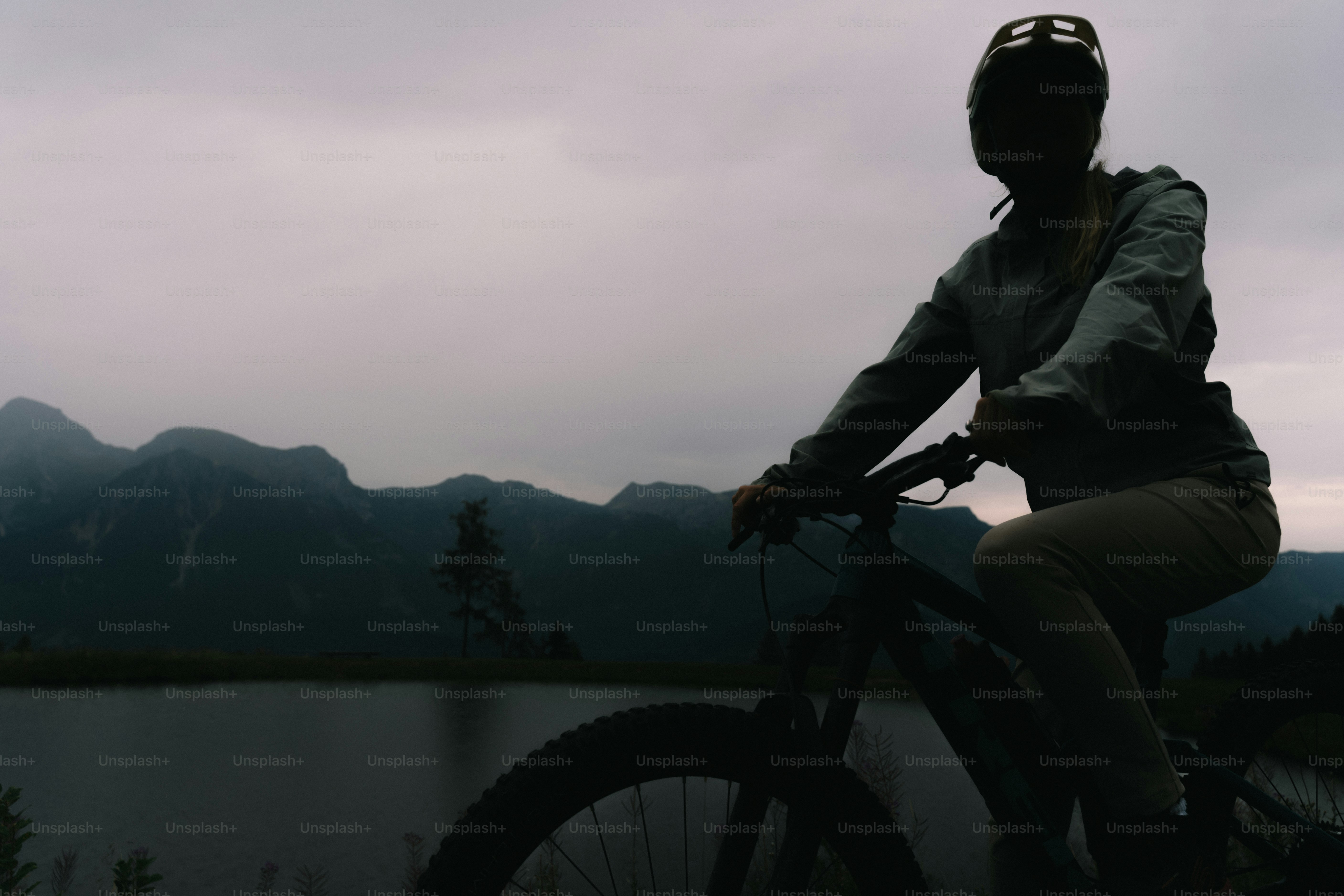 A person in silhouette on a mountain bike before a lake and mountains