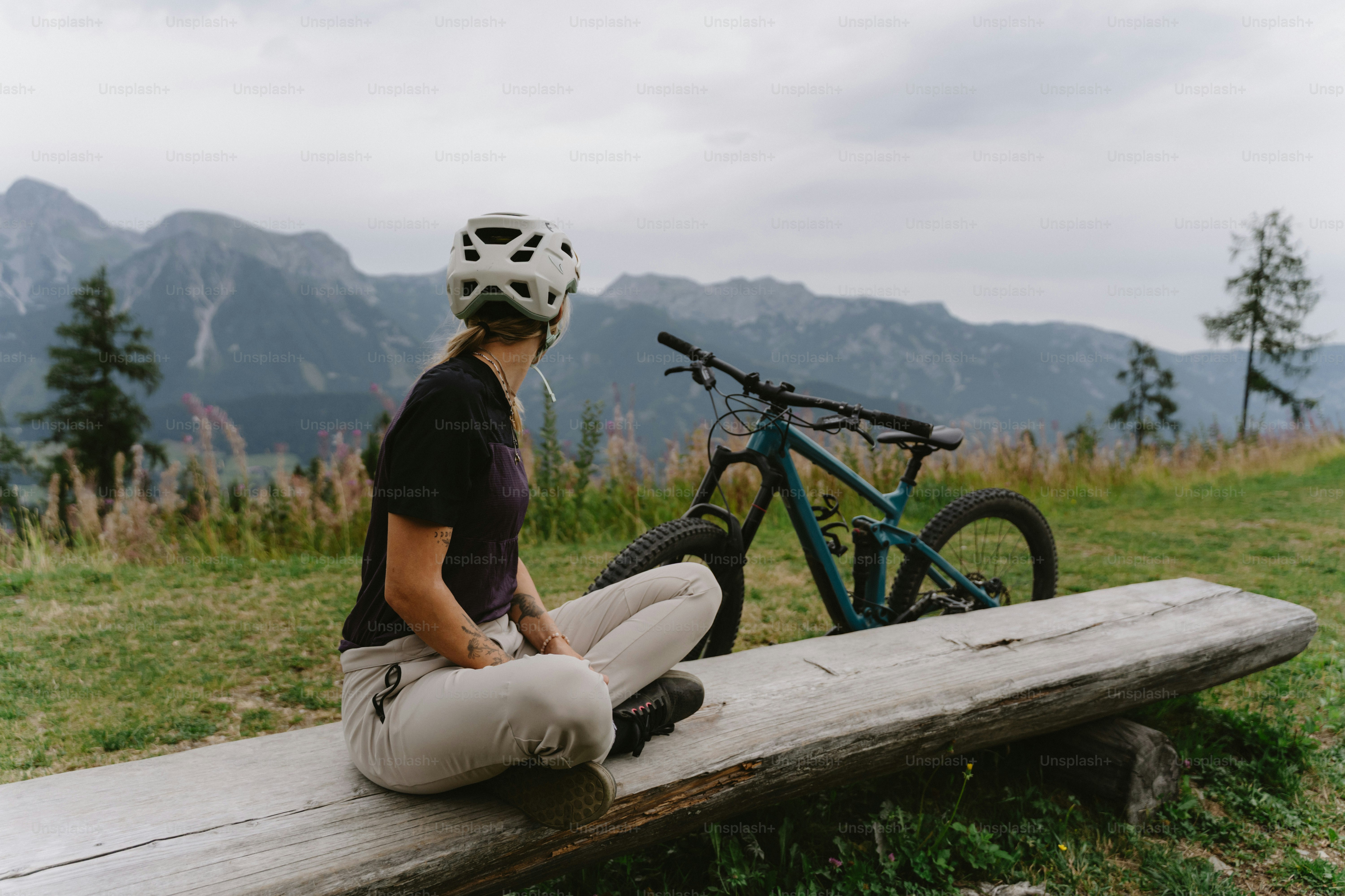 A person in a helmet sitting on a wooden bench with a mountain bike