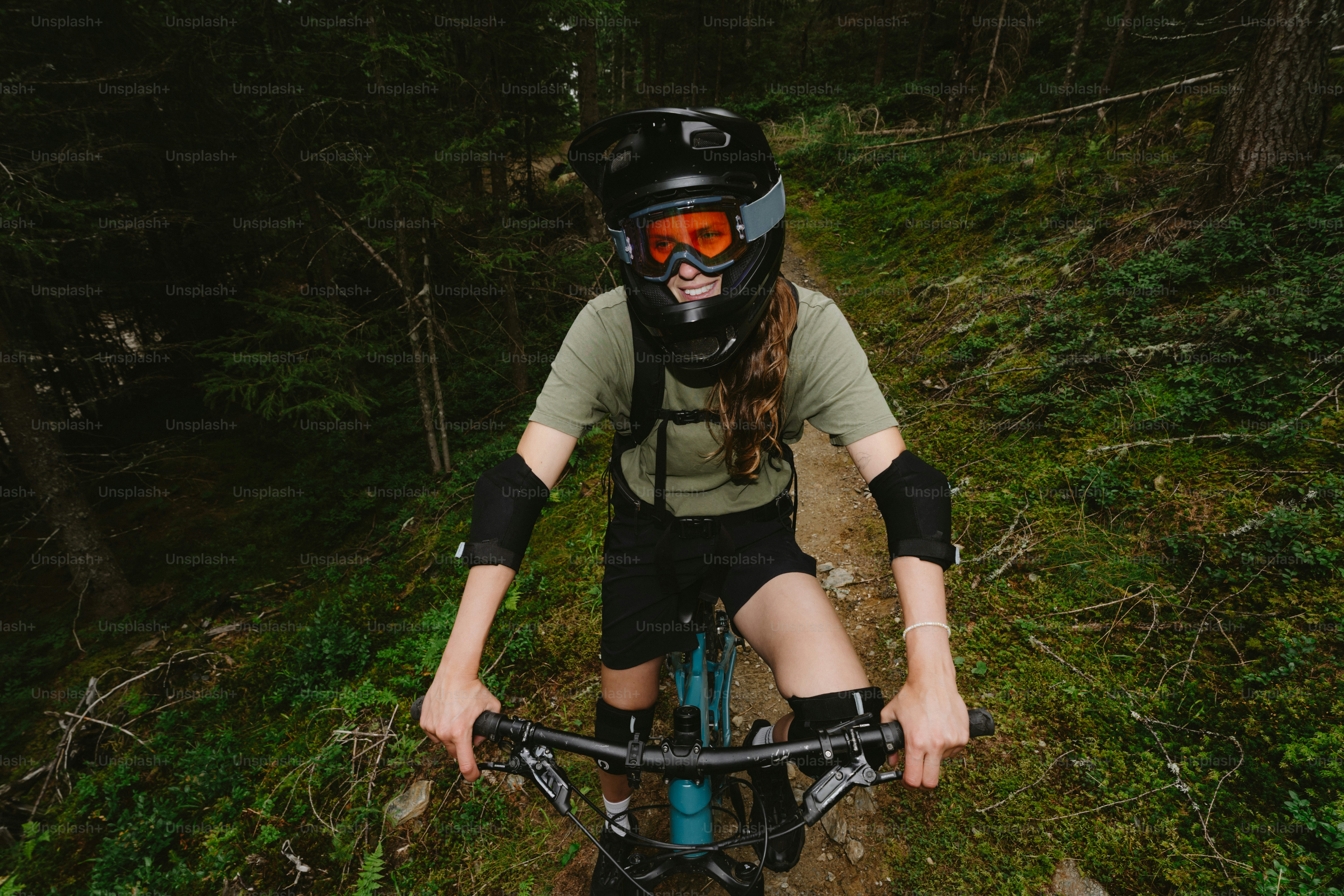 A mountain biker wearing a full-face helmet and pads on a forest trail