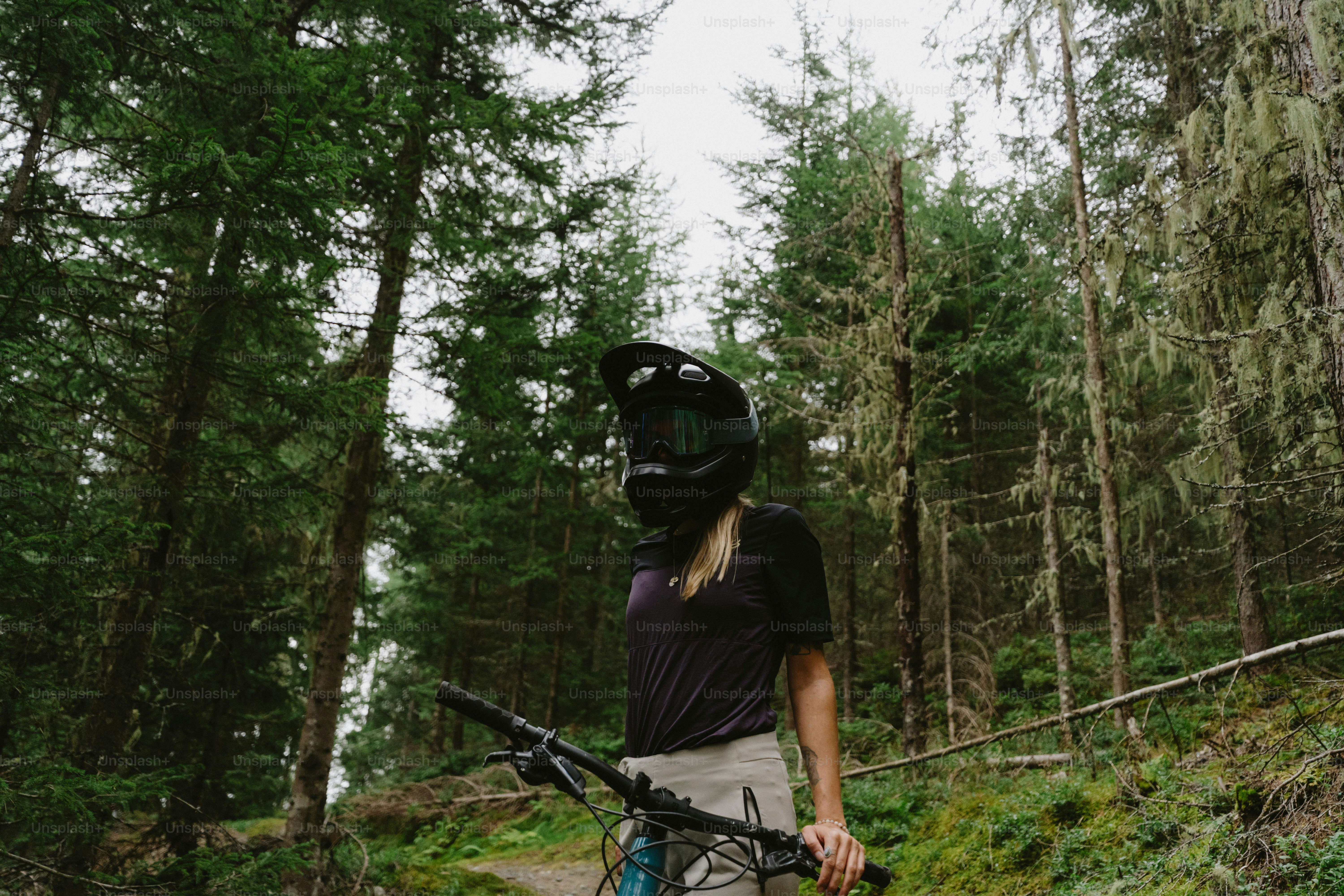 A person wearing a black helmet holding bicycle handlebars in a dense forest