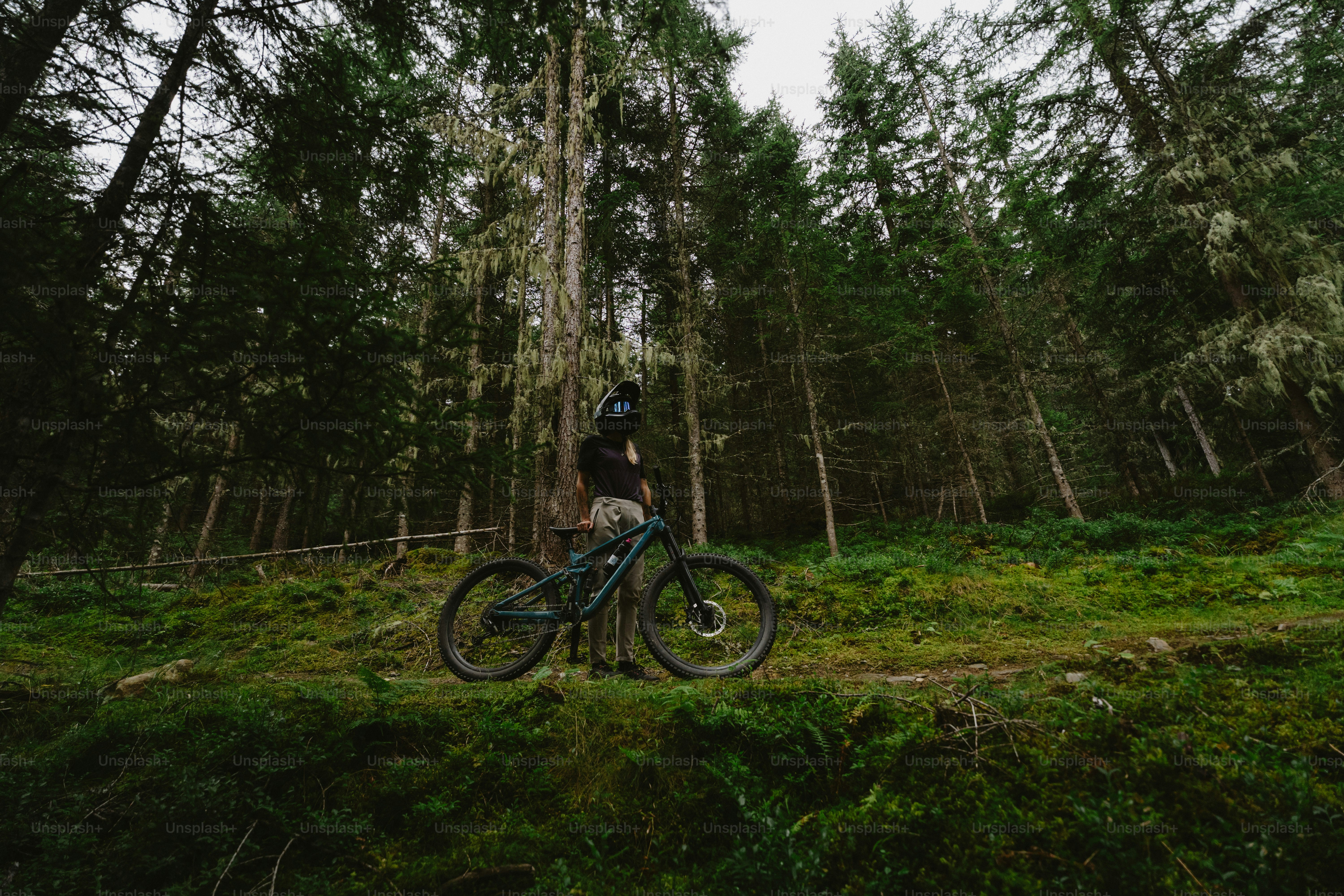 A person in a full-face helmet with a mountain bike in a dense forest