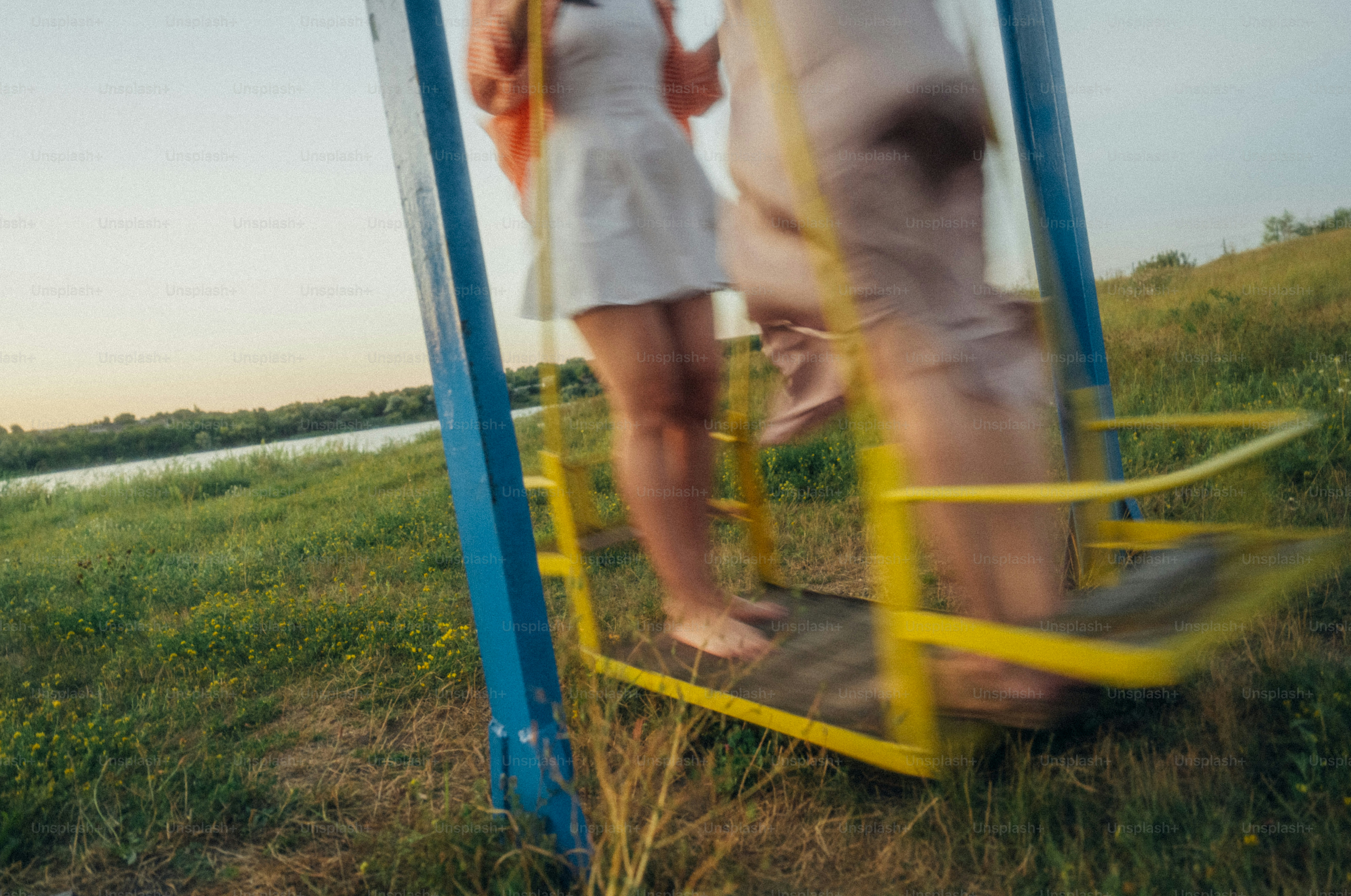 Two people on a yellow swing set in a grassy field at golden hour