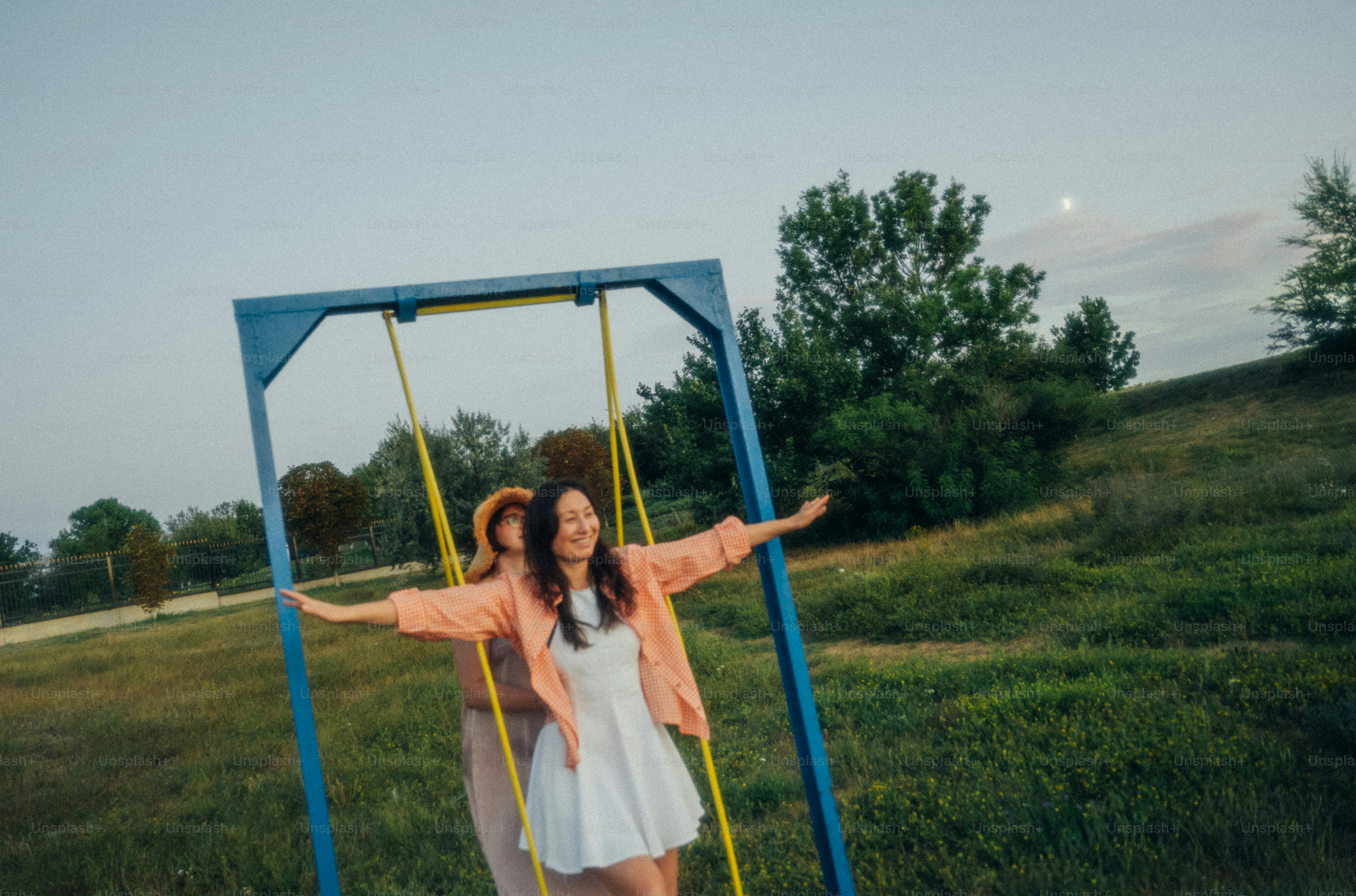 A woman in a white dress and orange shirt on a swing outdoors