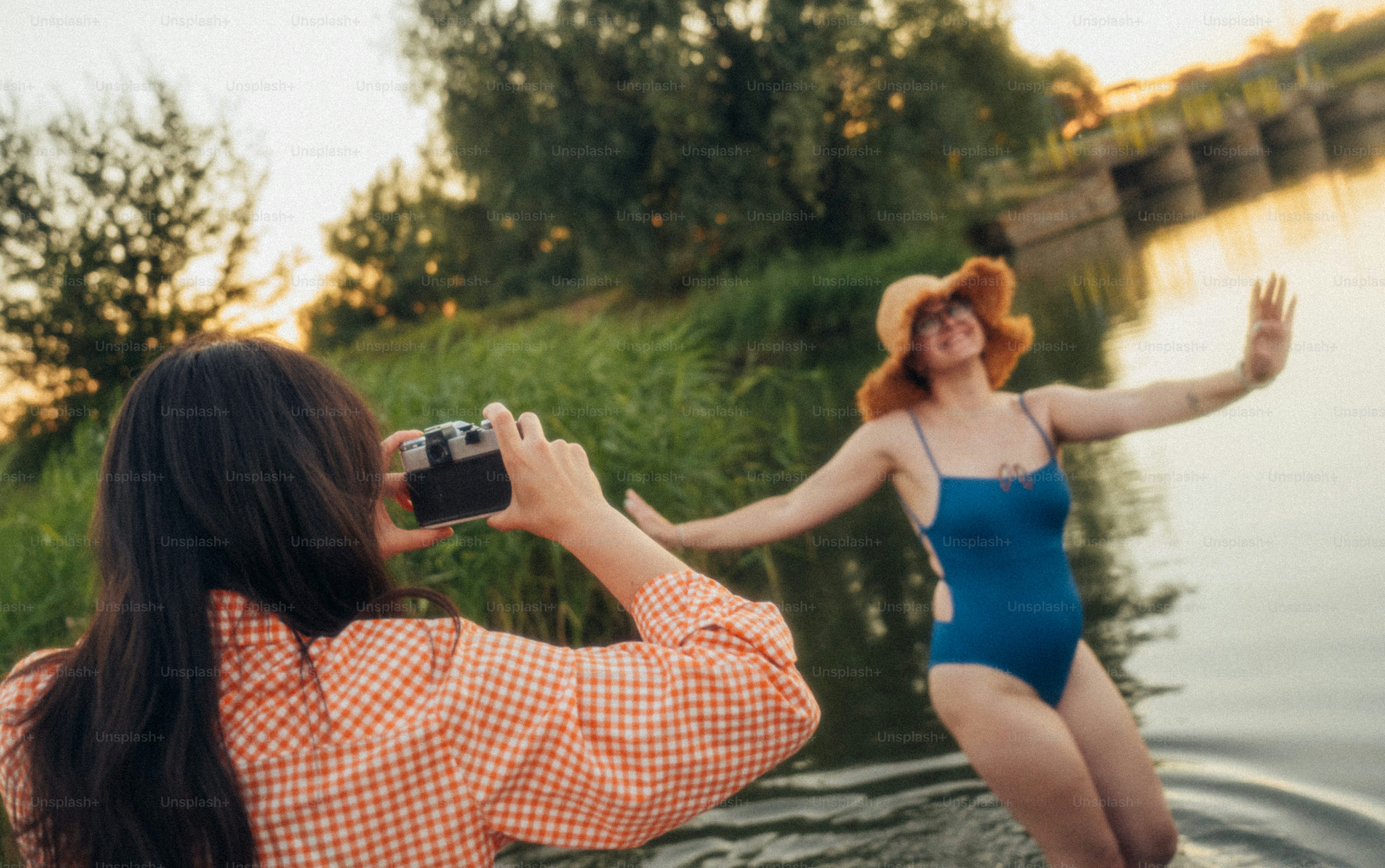 A person in an orange plaid shirt photographing a woman in a blue swimsuit