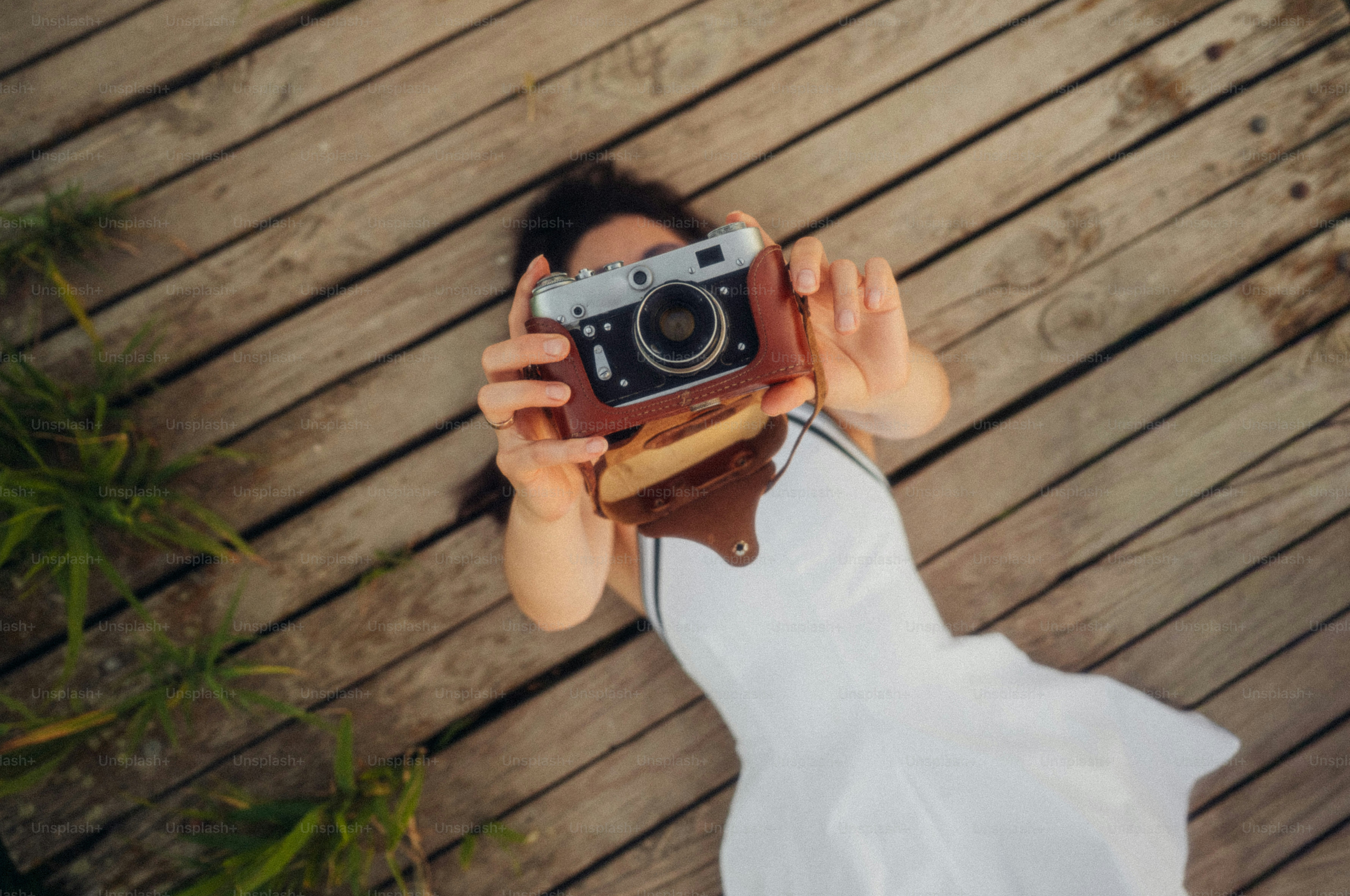 A woman in a white dress holding a vintage camera on wooden planks