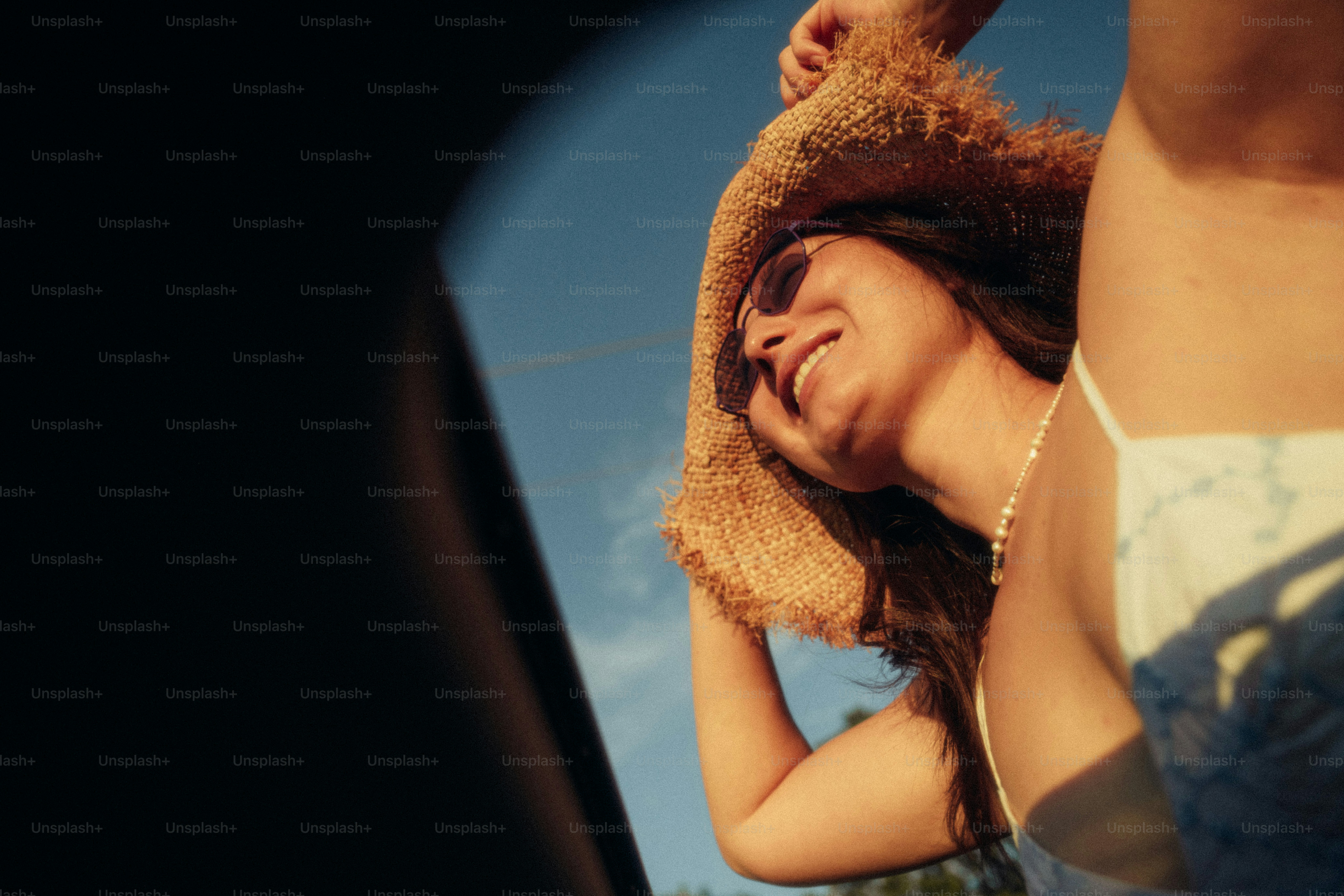 A woman in a straw hat and sunglasses smiling against a blue sky