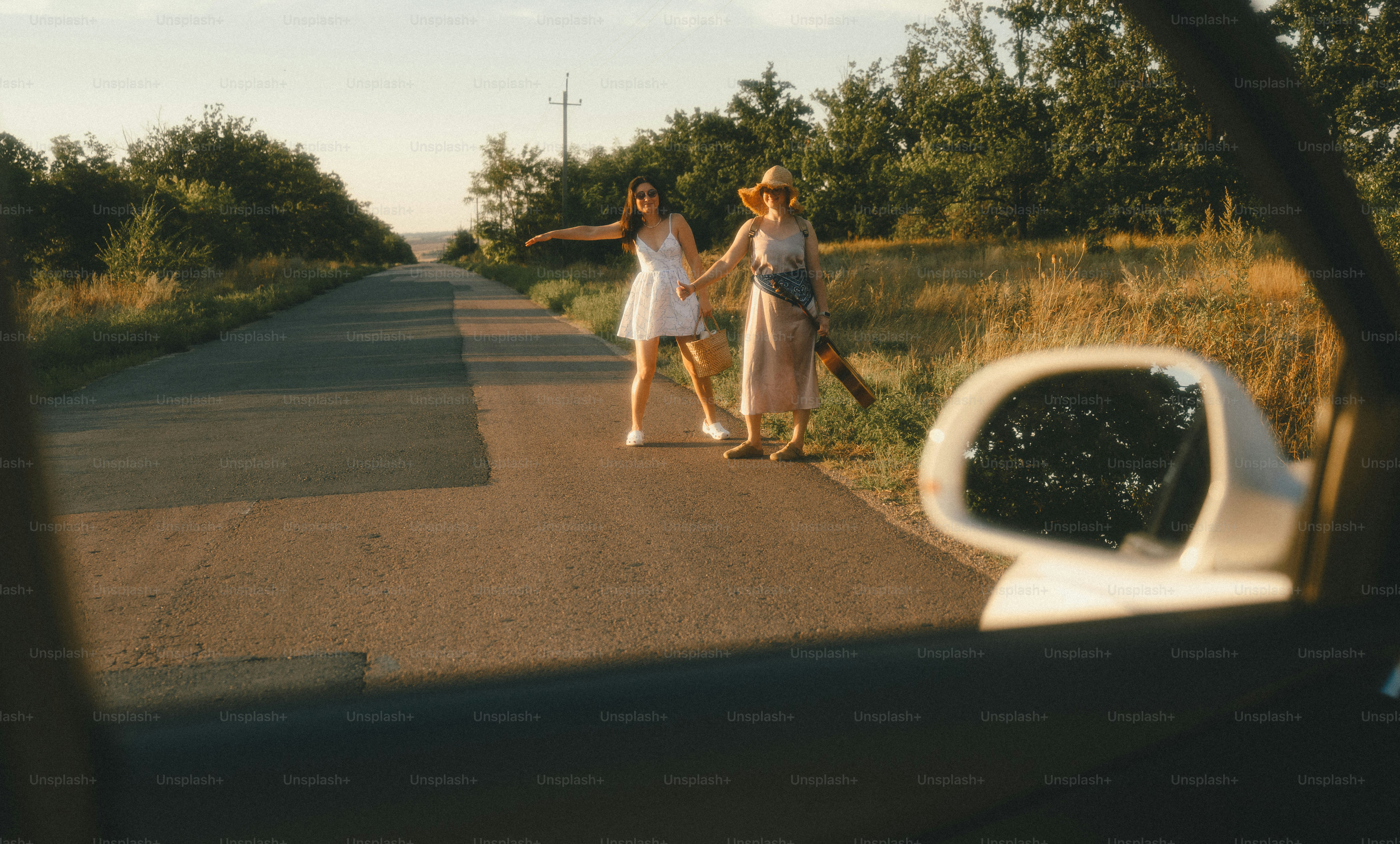 Two women hitchhiking on a rural road during the golden hour