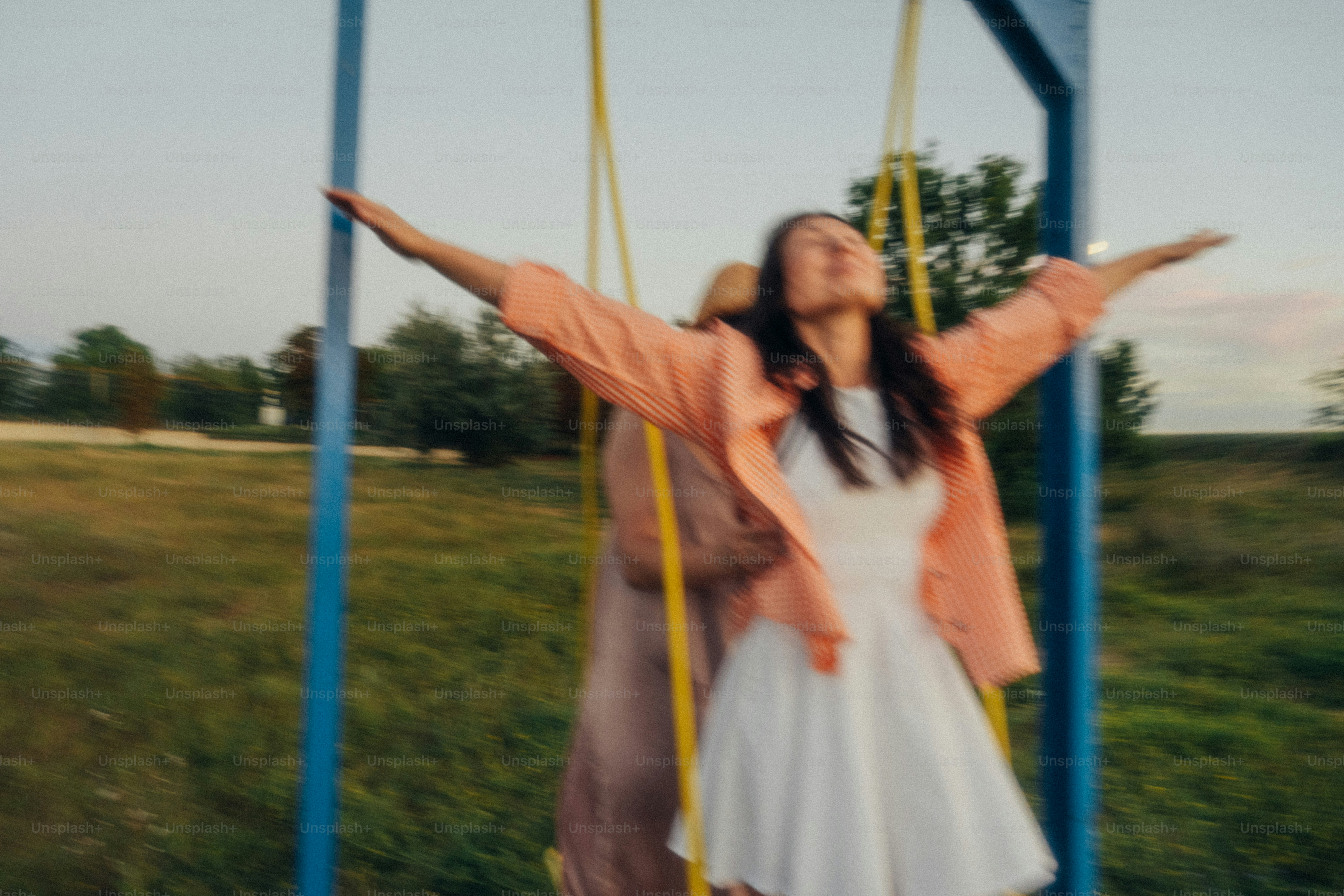 A woman in a white dress and orange shirt swinging on a playground swing