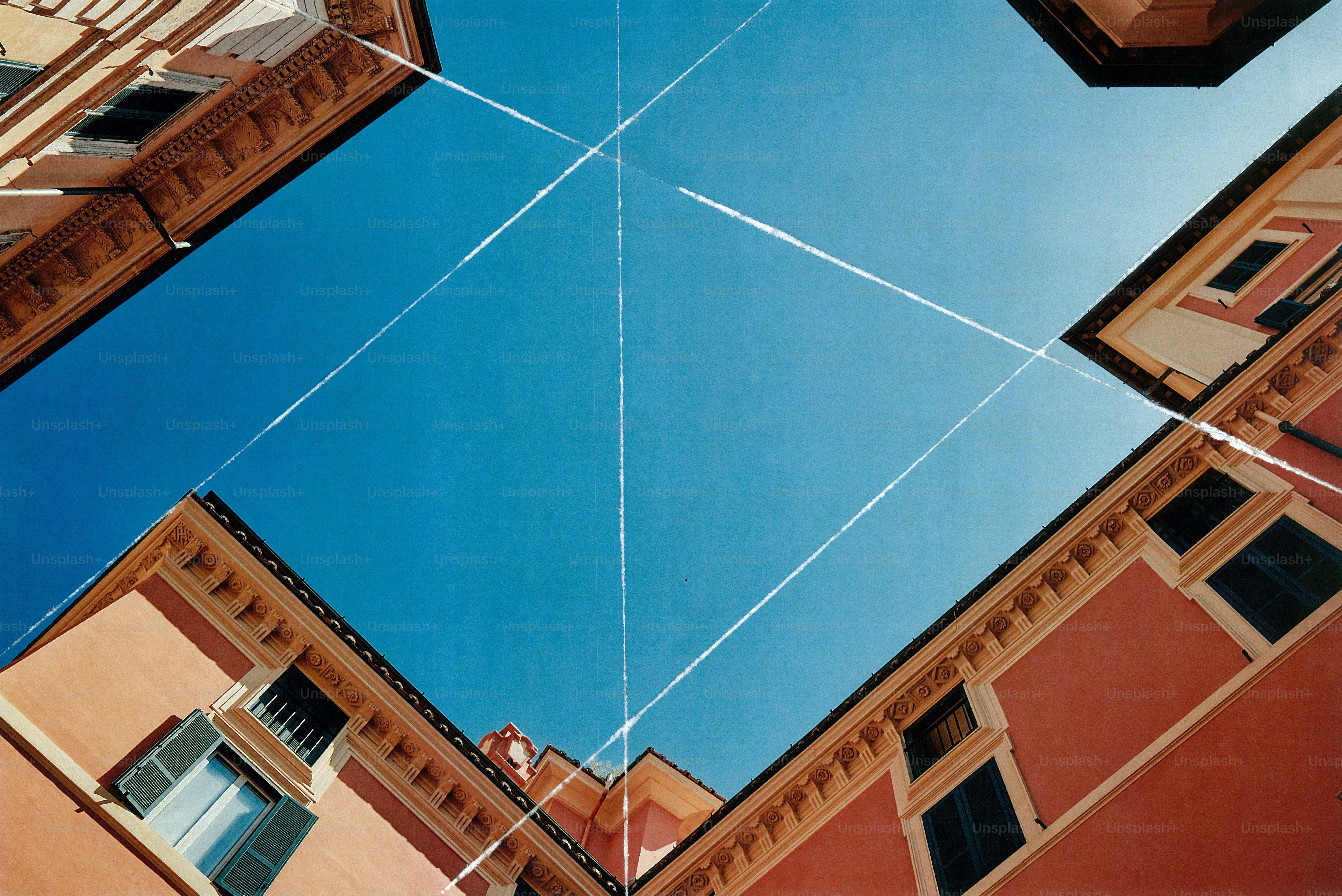 Vista a bassa angolazione di edifici in terracotta che incorniciano un cielo azzurro brillante con scie di vapore che si intersecano