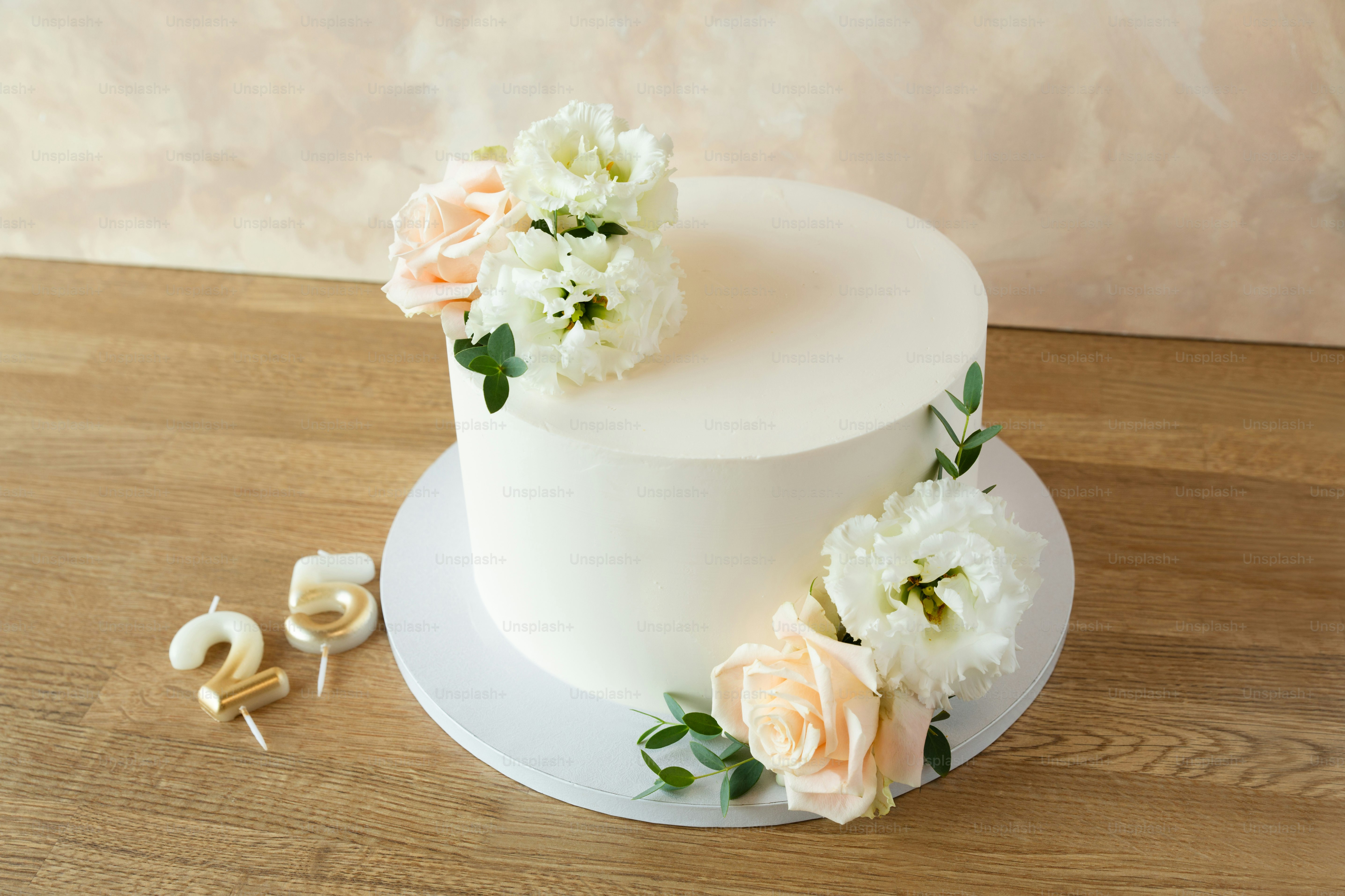 Una torta bianca glassata decorata con rose pallide e fiori bianchi su un tavolo di legno