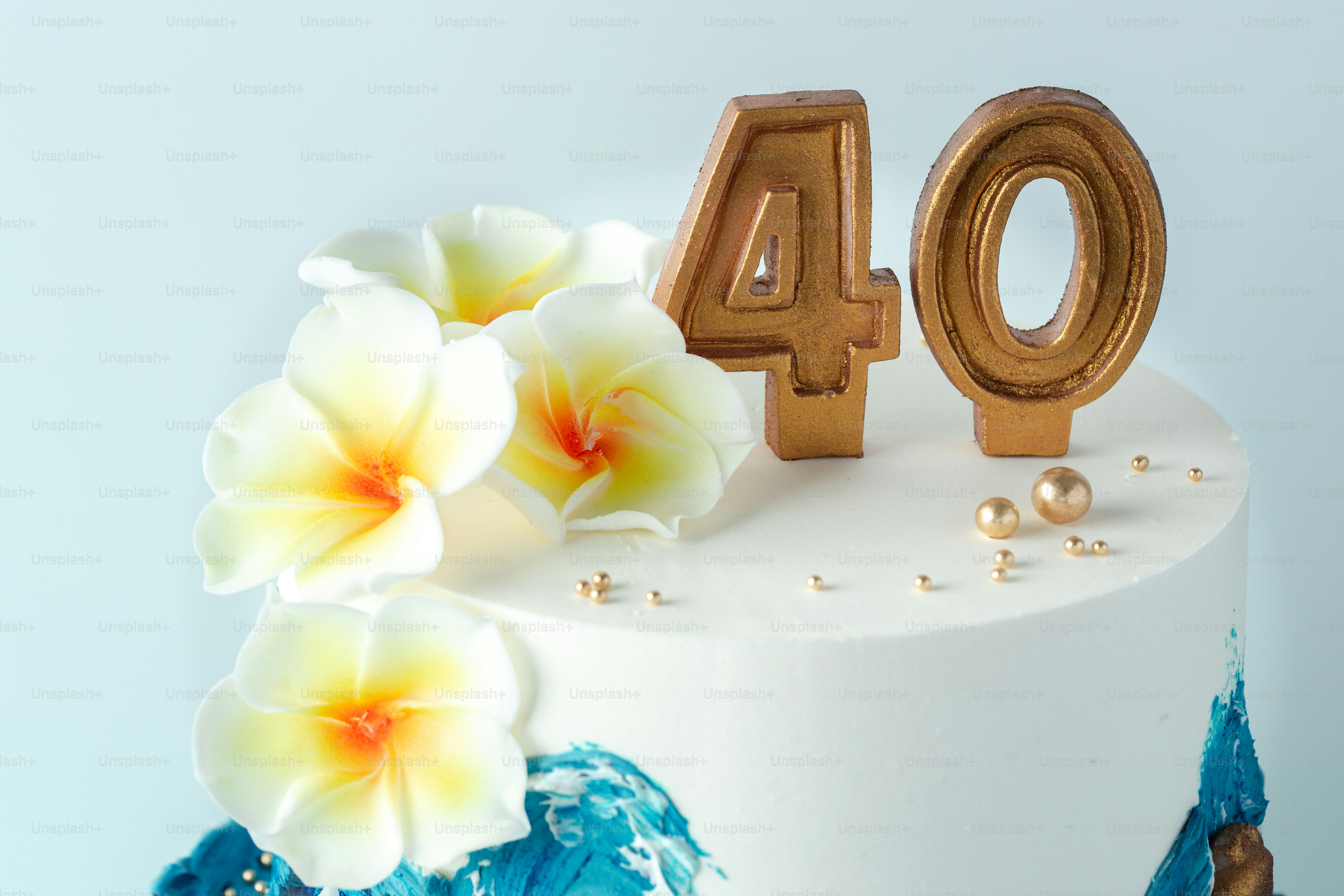 Una torta bianca decorata con fiori di plumeria bianca e candele dorate numero quaranta