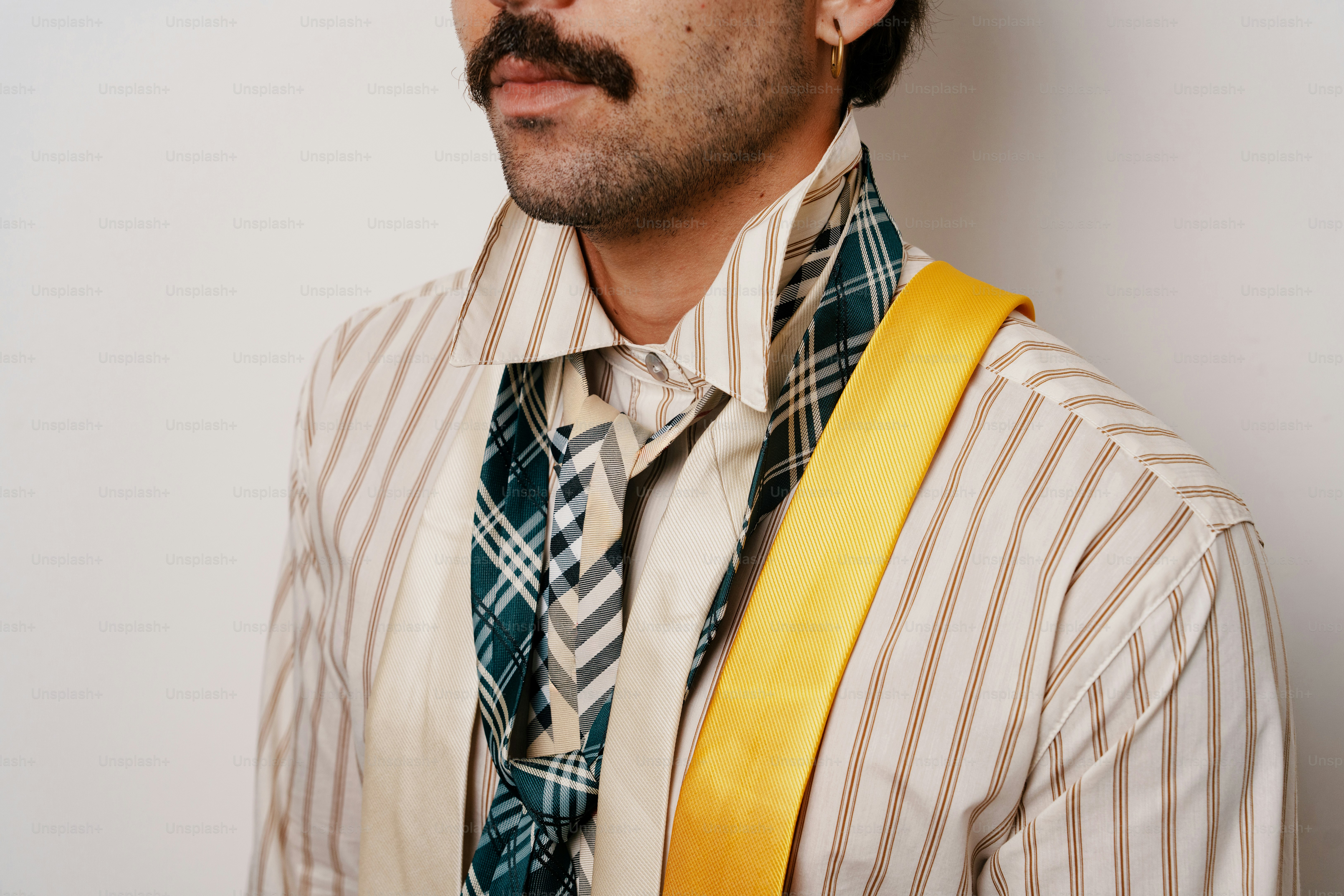A person with a mustache wearing a striped shirt and multiple layered neckties