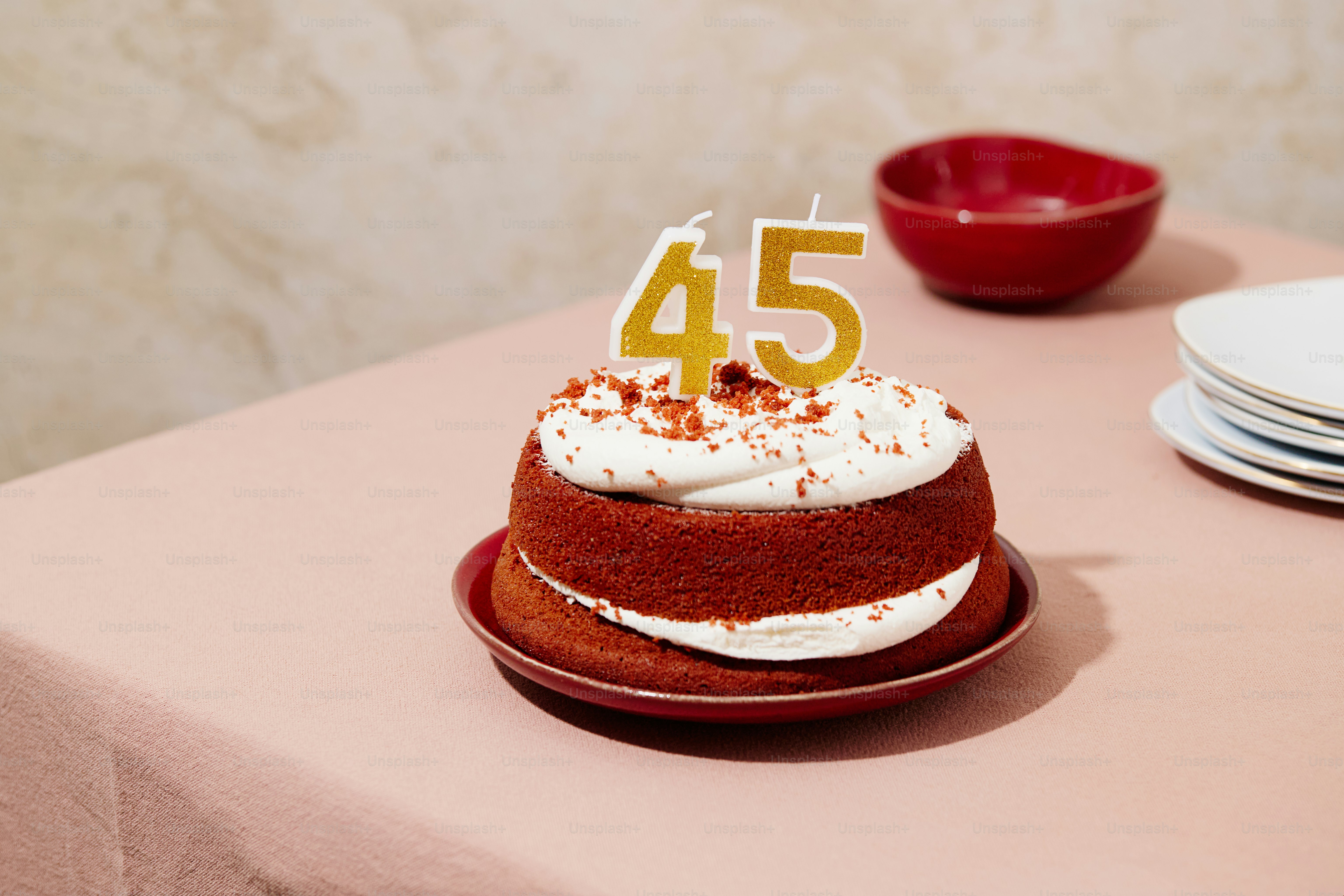 A red velvet cake with white frosting and gold number 45 candles