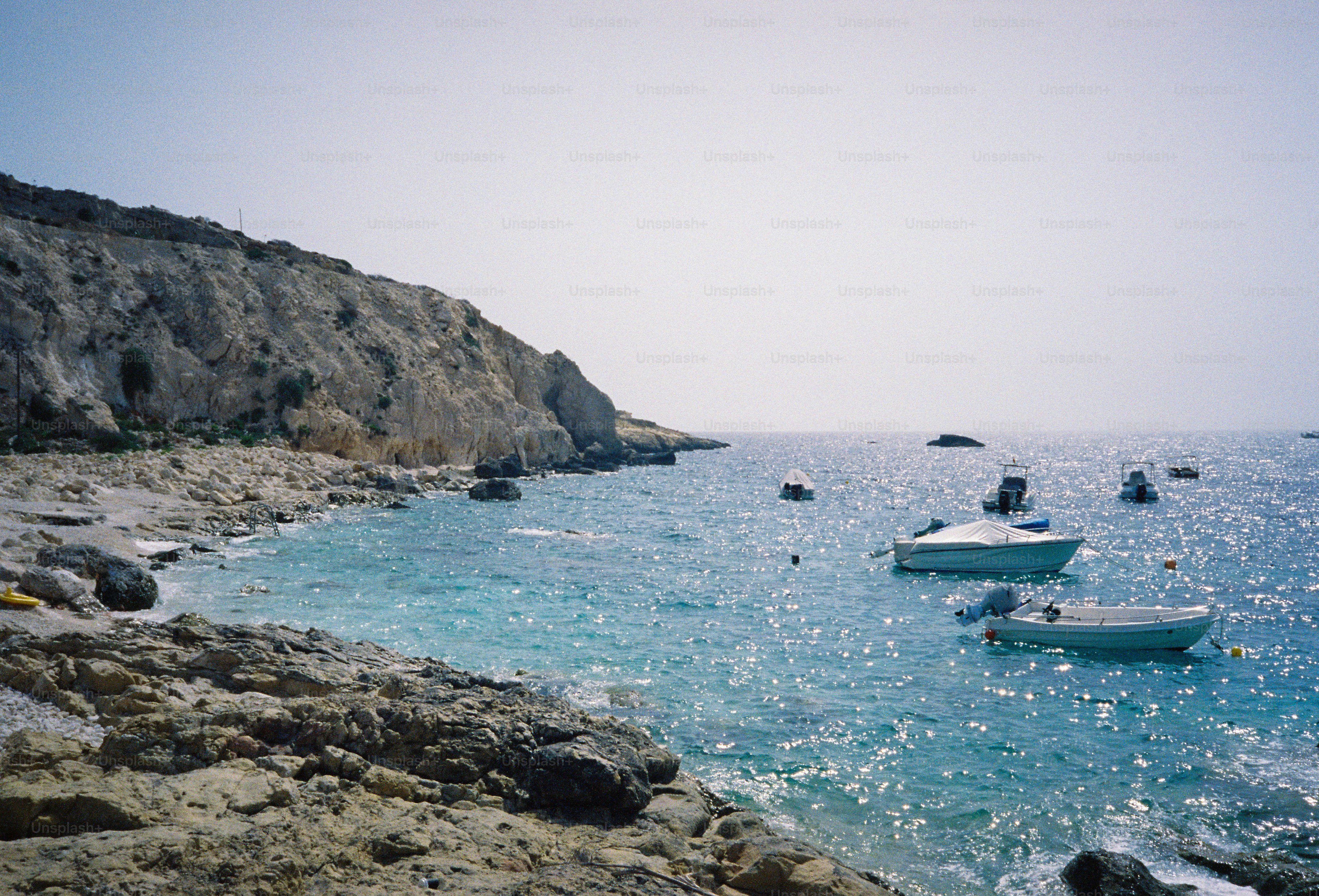 Small boats anchored in a turquoise bay beside a rocky coastline