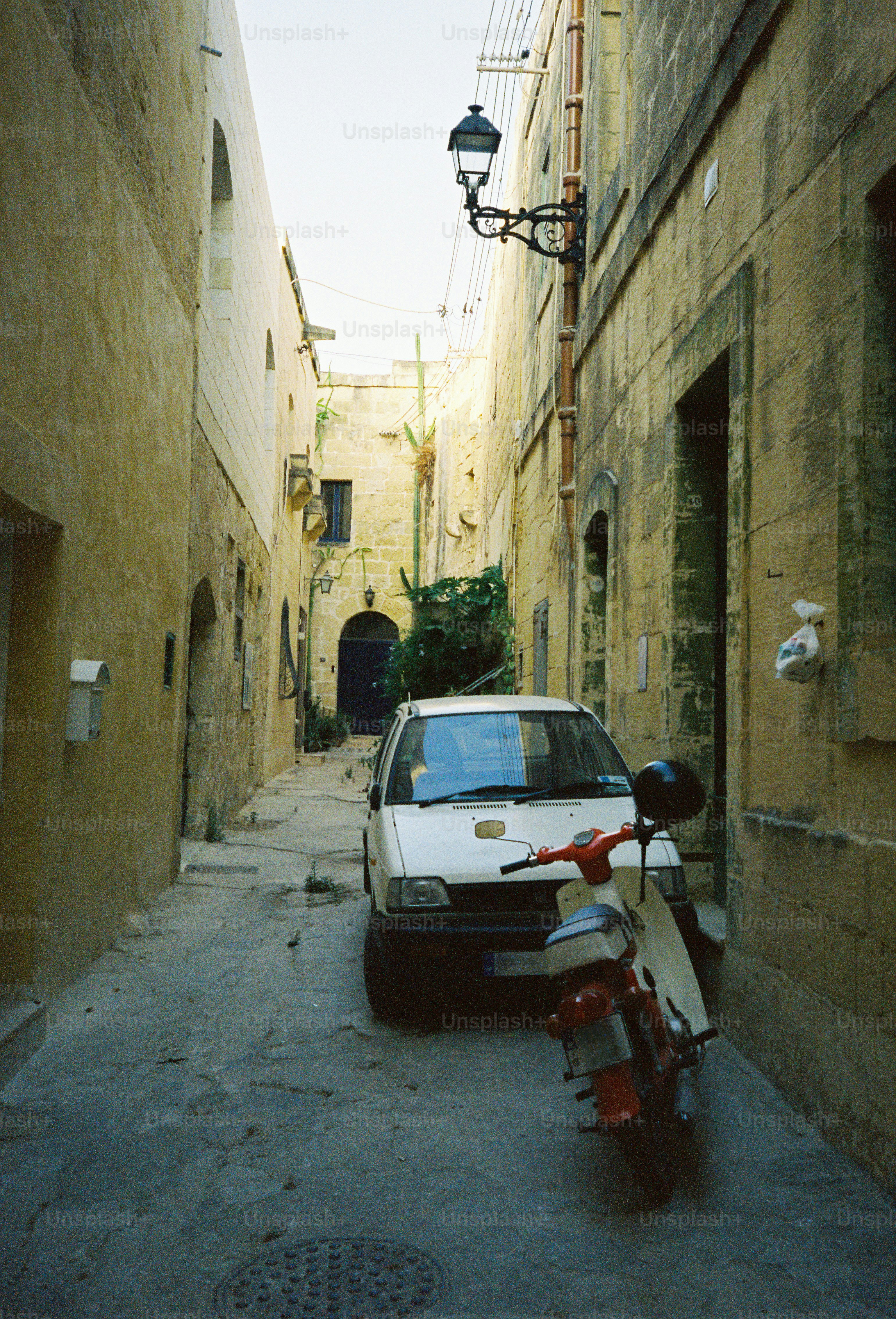 A white car and a red scooter parked in a narrow stone alleyway