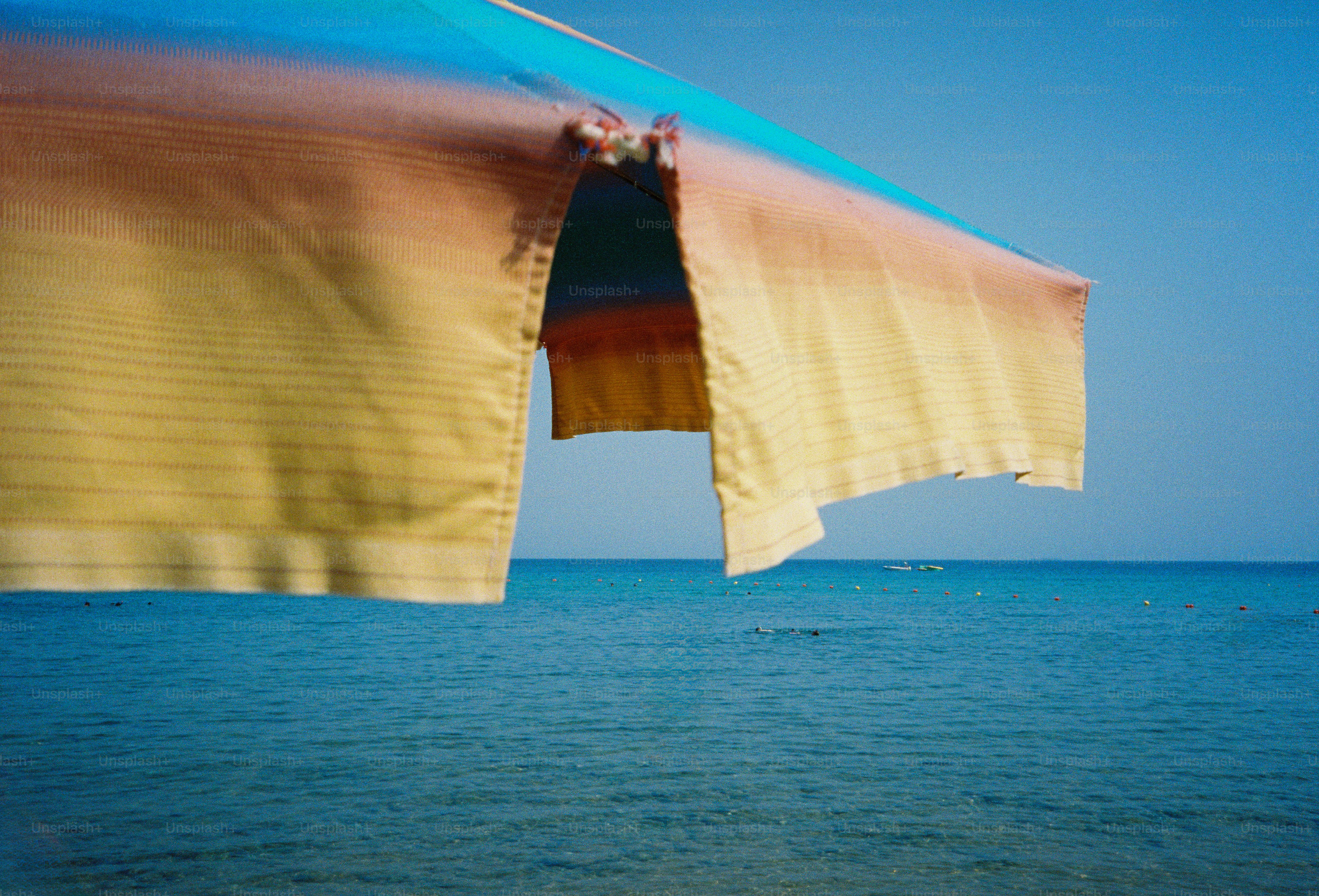 A colorful beach umbrella against a clear blue sky and calm ocean water