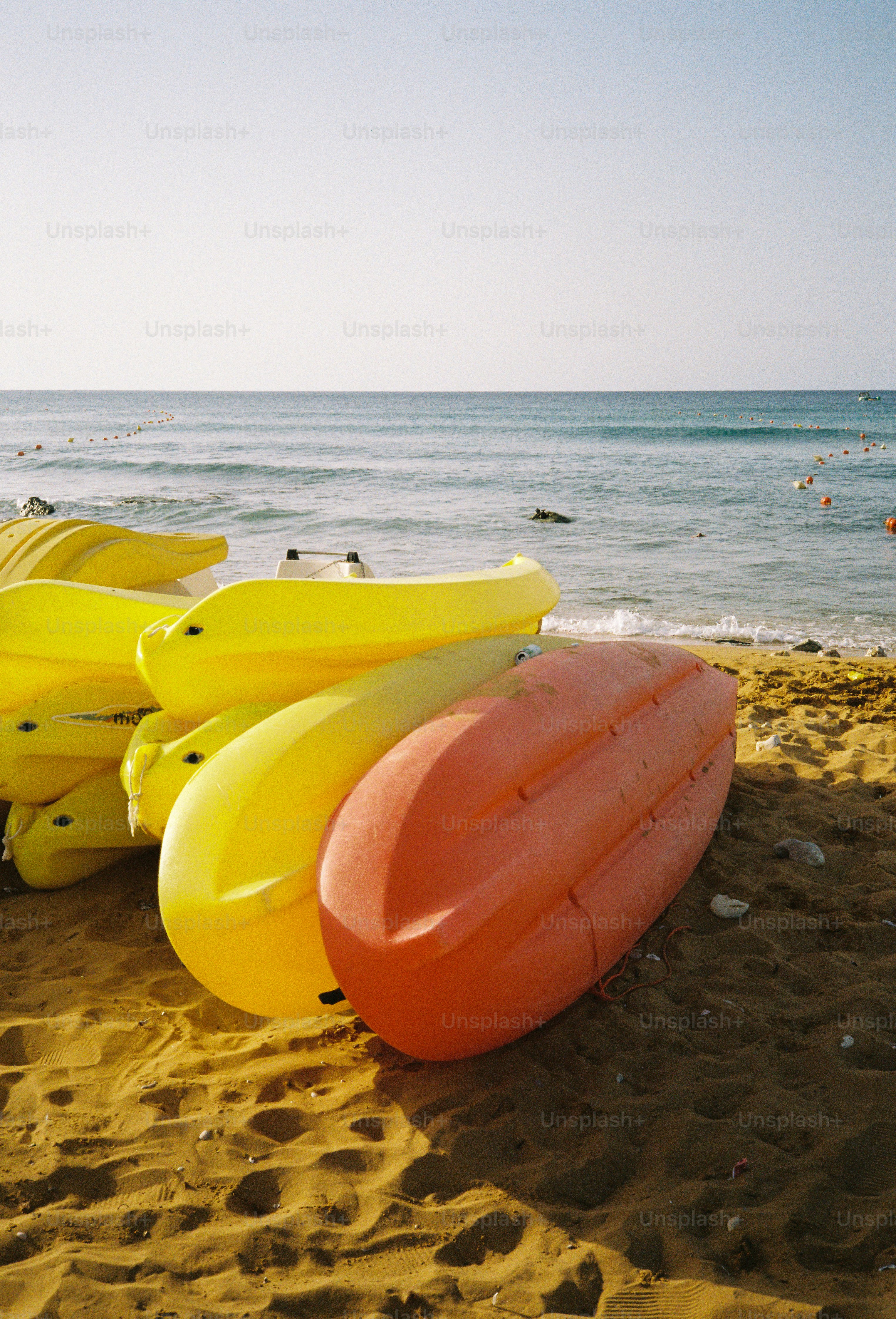 A stack of yellow and orange kayaks on a sandy beach by the sea