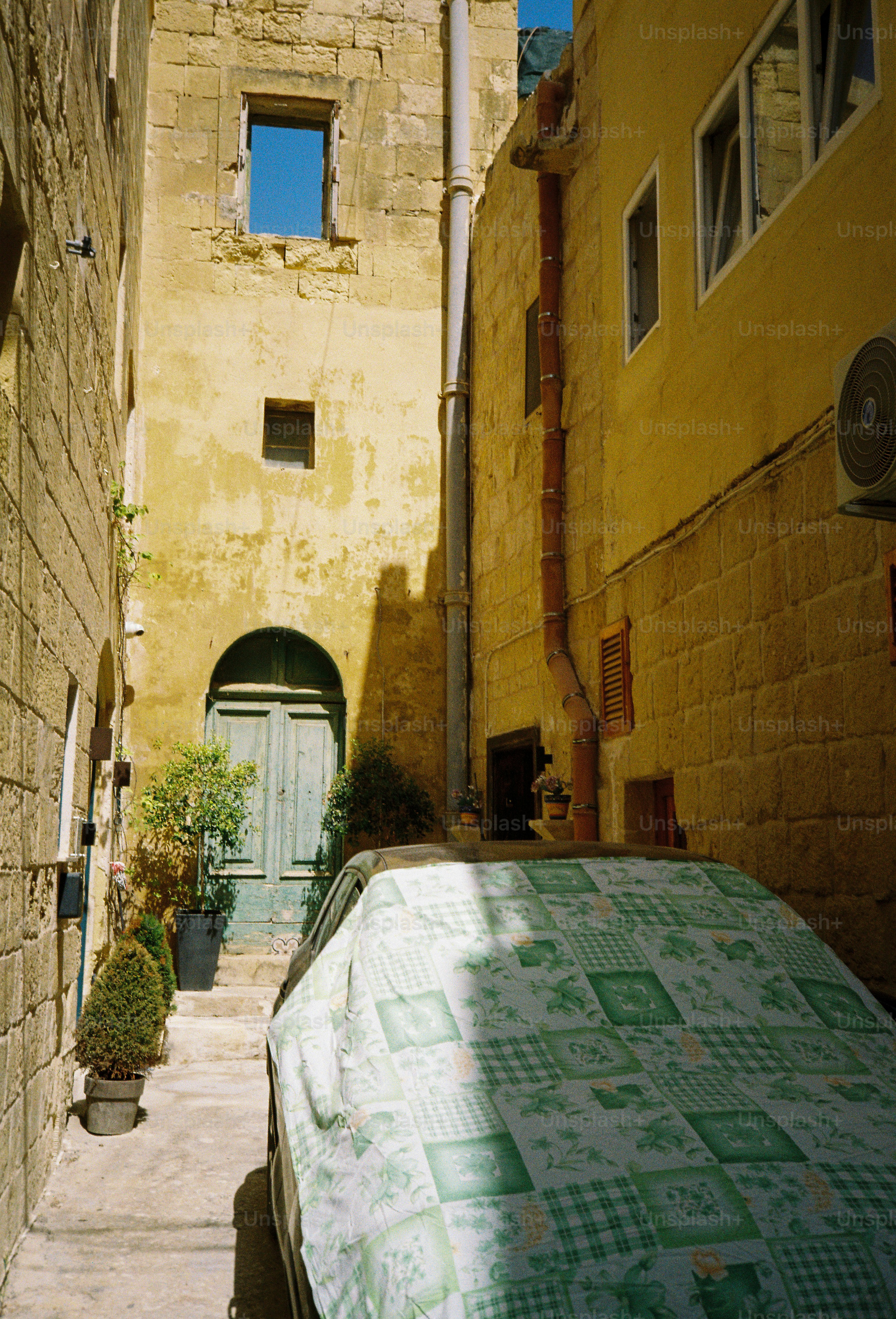 A car covered with a green patterned cloth in a narrow stone alleyway