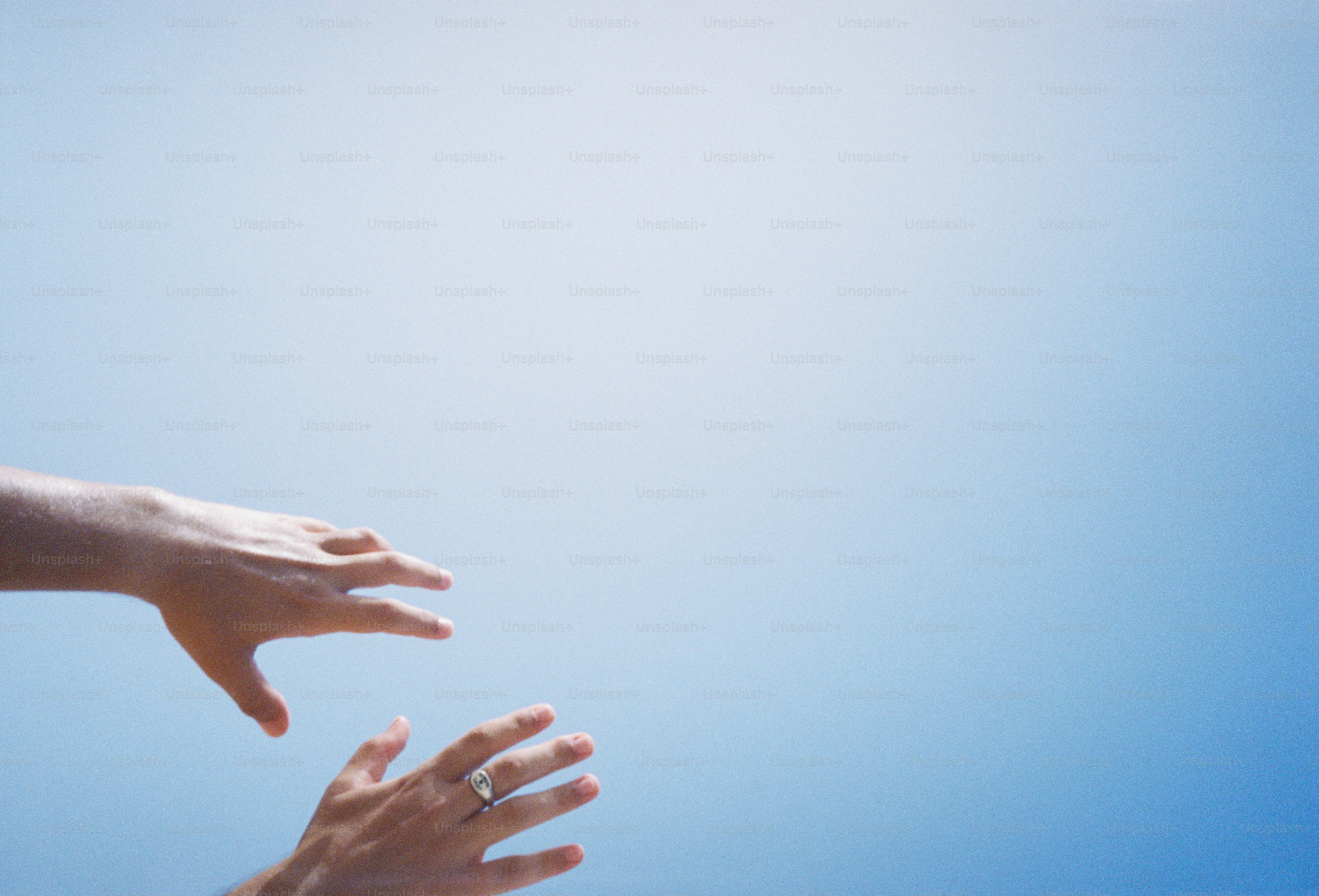 Two hands reaching upward against a clear bright blue sky