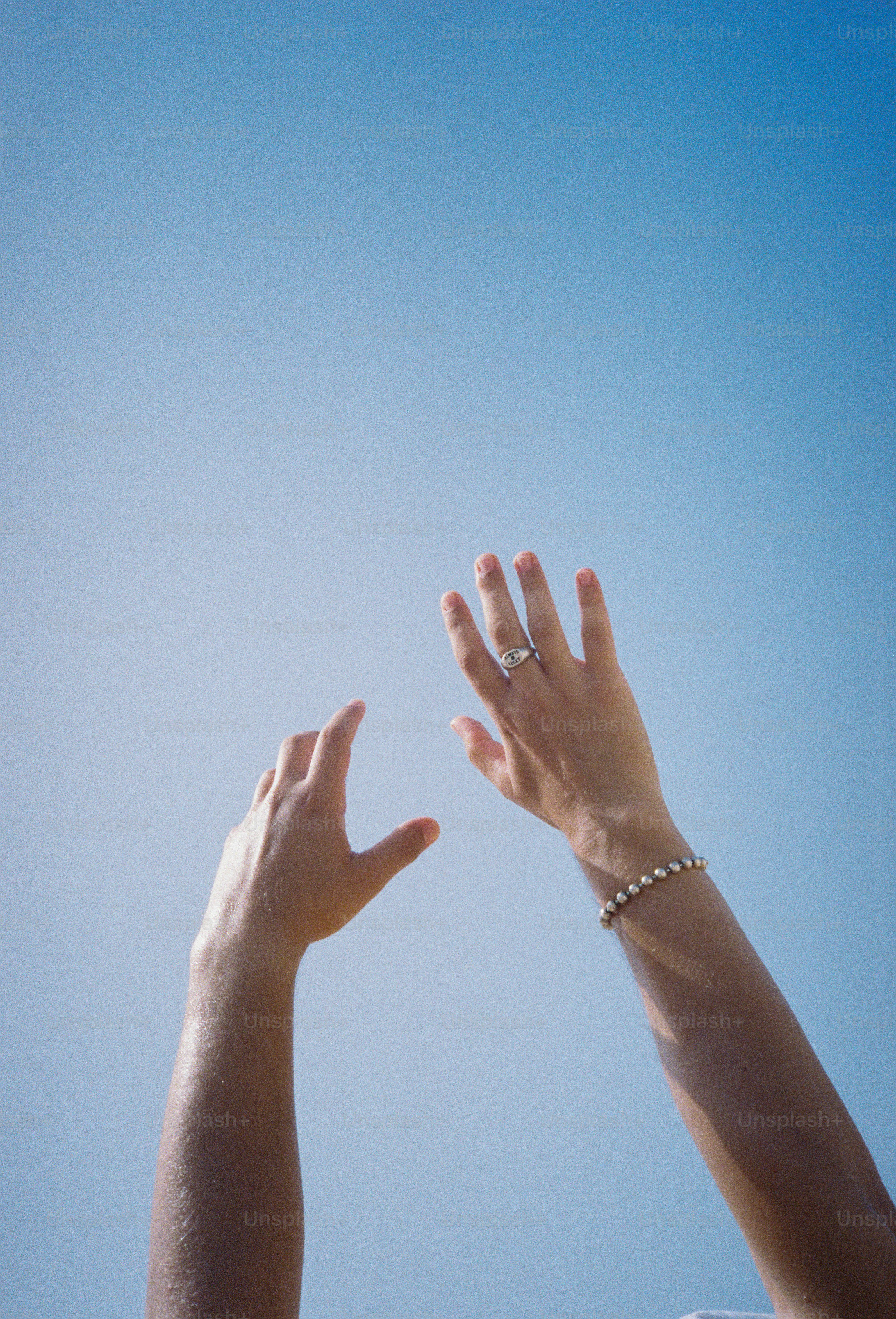 Two hands reaching upward toward a clear blue sky