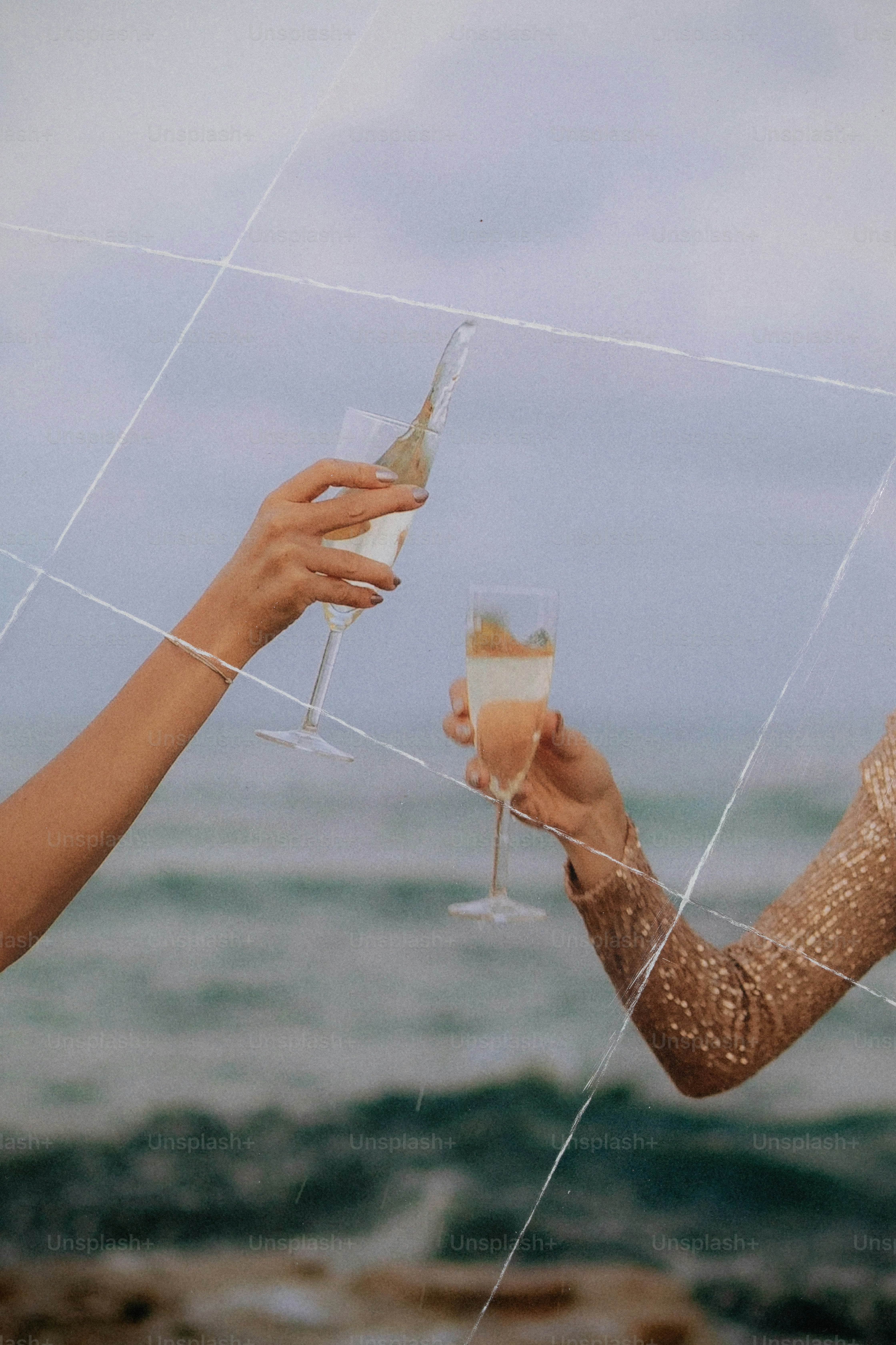 Two people holding champagne flutes for a toast against a blurred ocean background