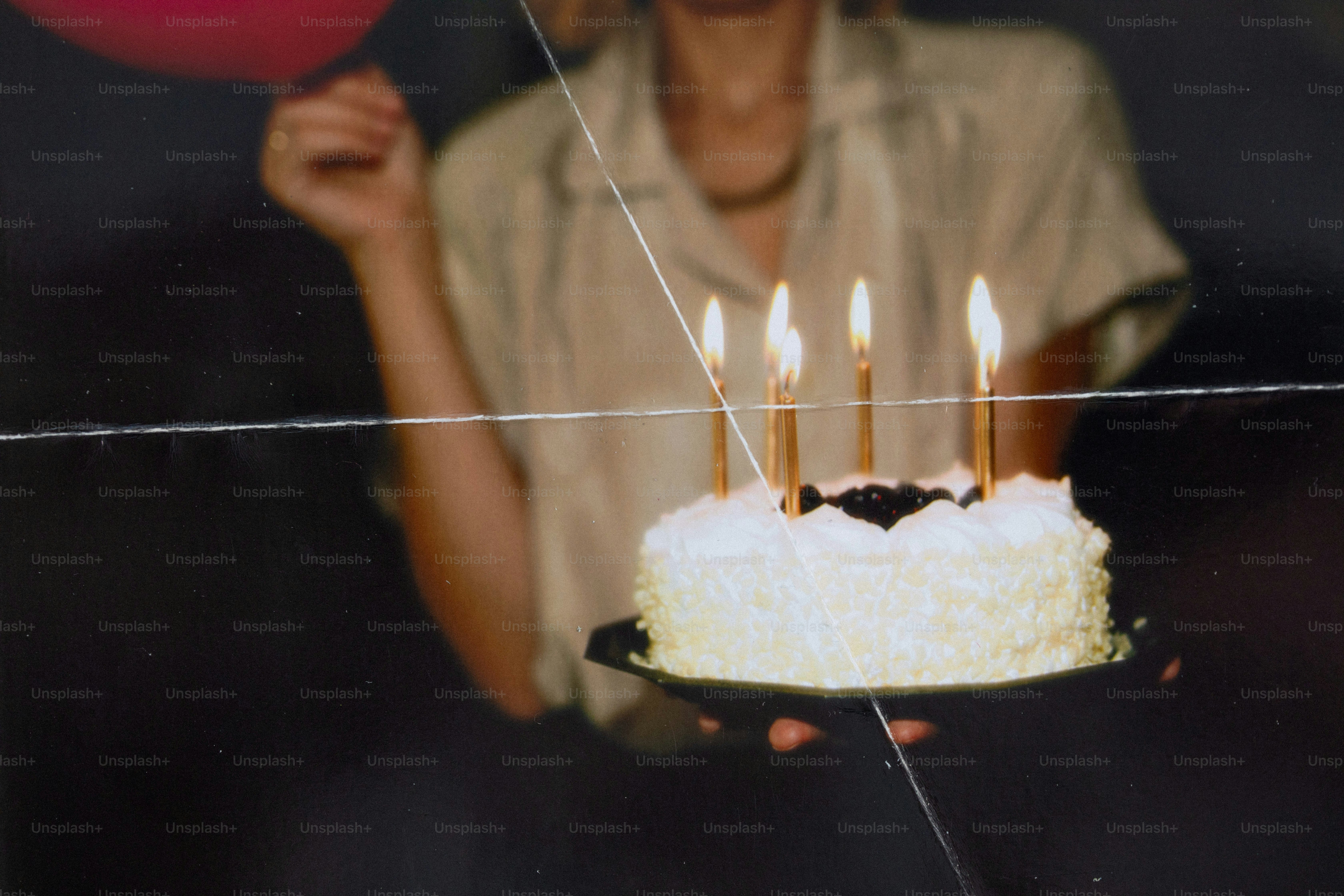 A person holding a birthday cake with five lit candles in a dark room
