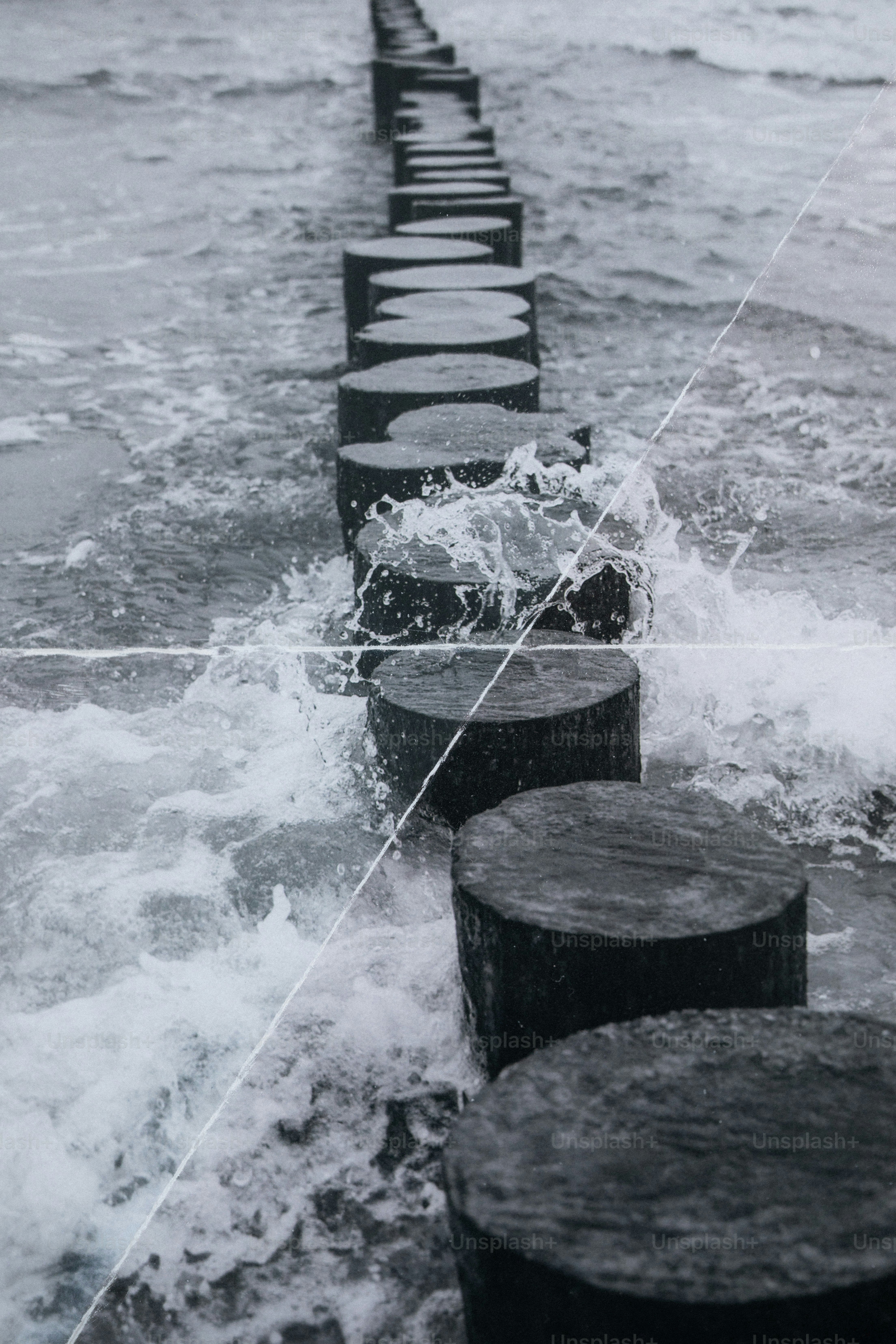 Waves crashing against a line of wooden posts in the sea