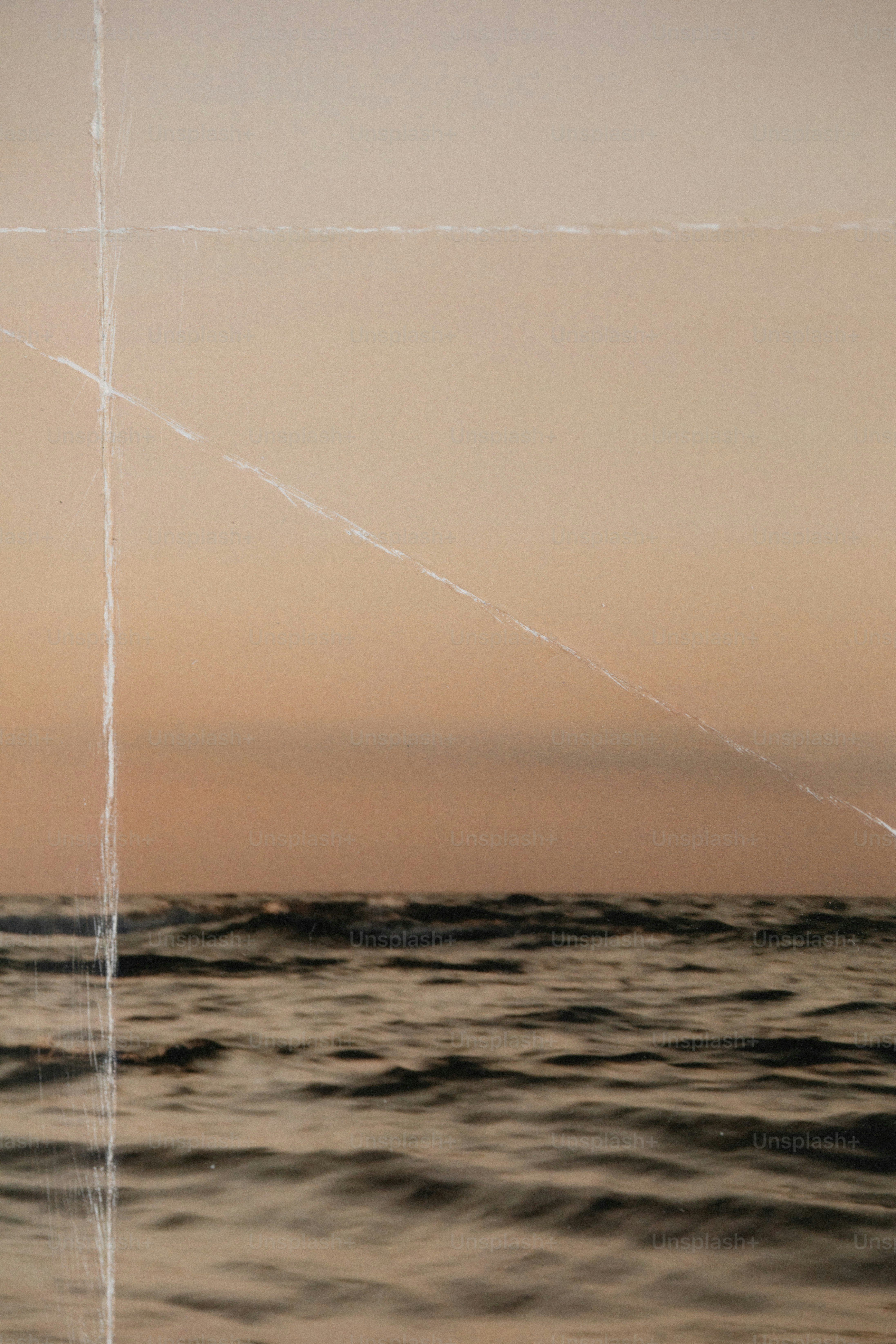 A textured overlay with white scratches over a calm sea at golden hour
