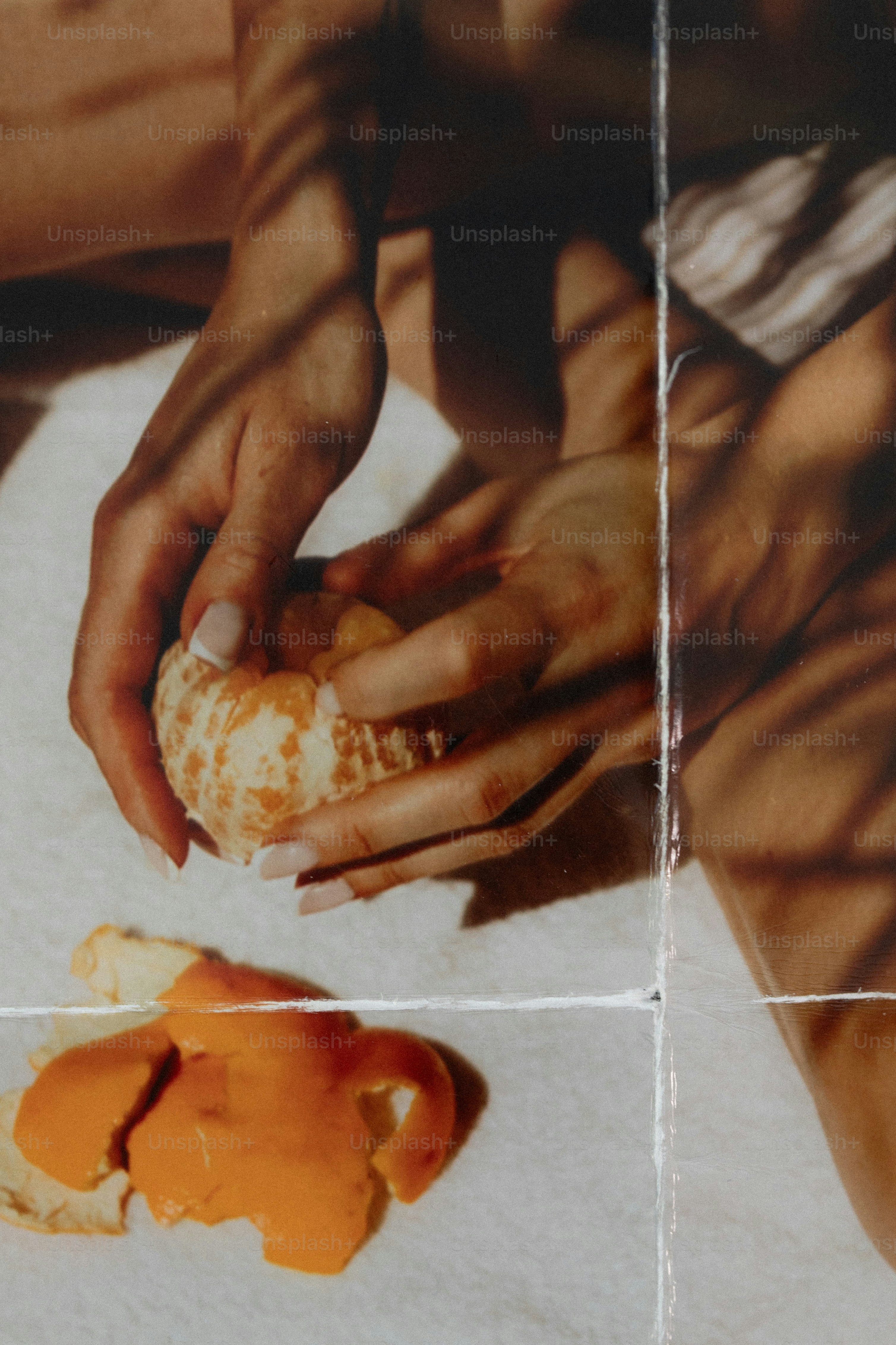 Hands peeling a fresh orange with discarded peel on a white surface
