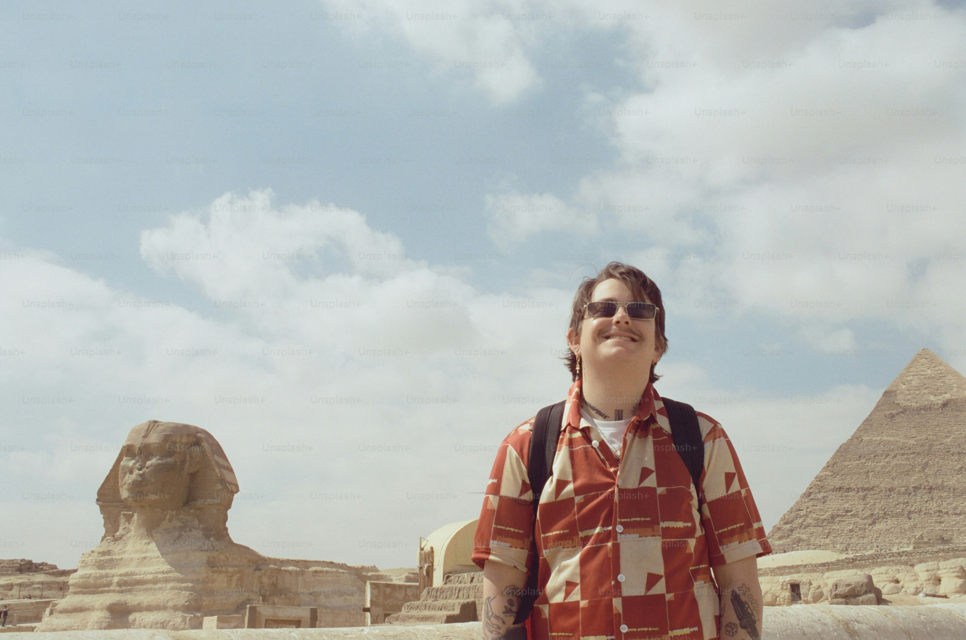 A person in a patterned shirt and sunglasses before the Great Sphinx in Giza