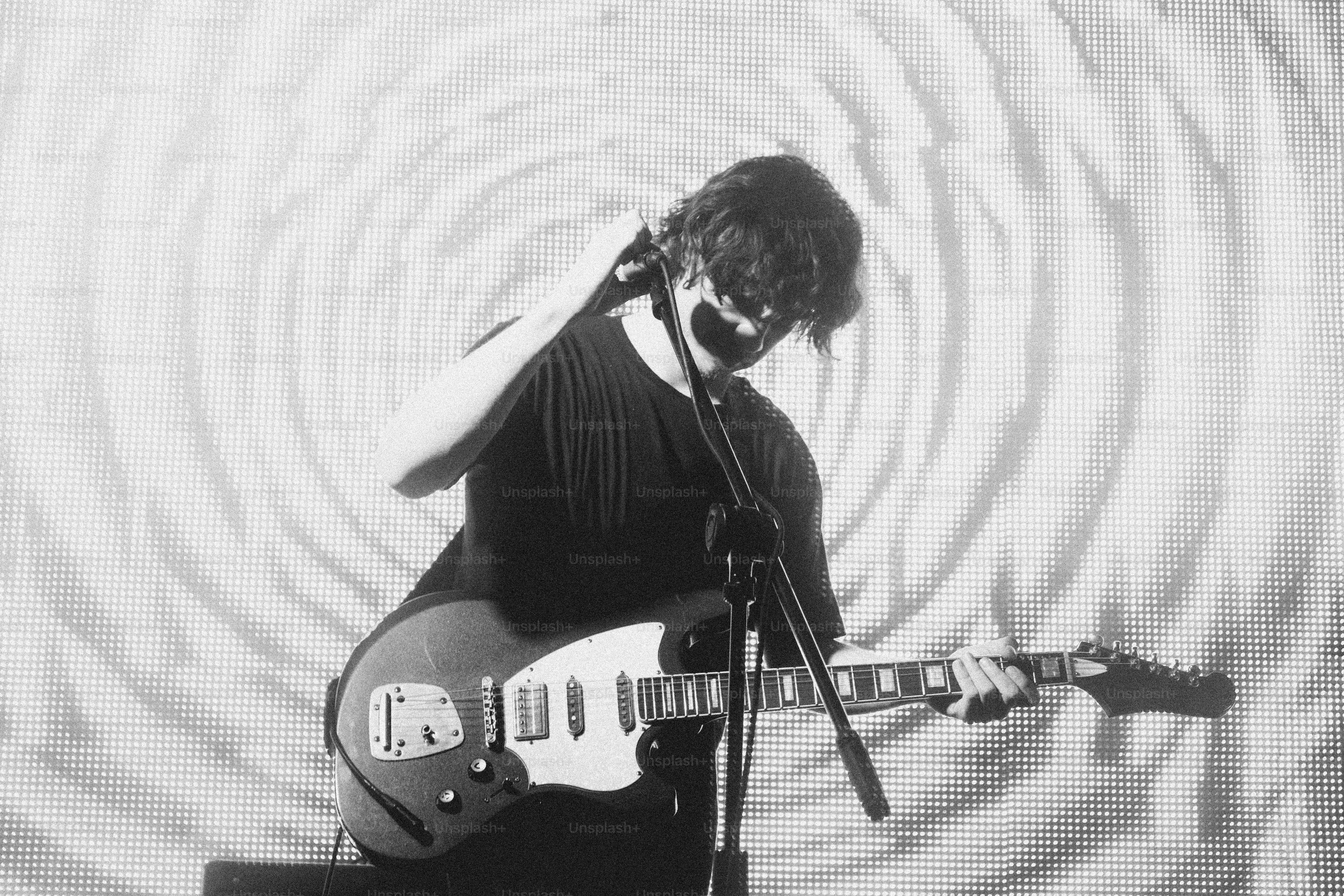 A person playing an electric guitar on stage in front of a circular pattern