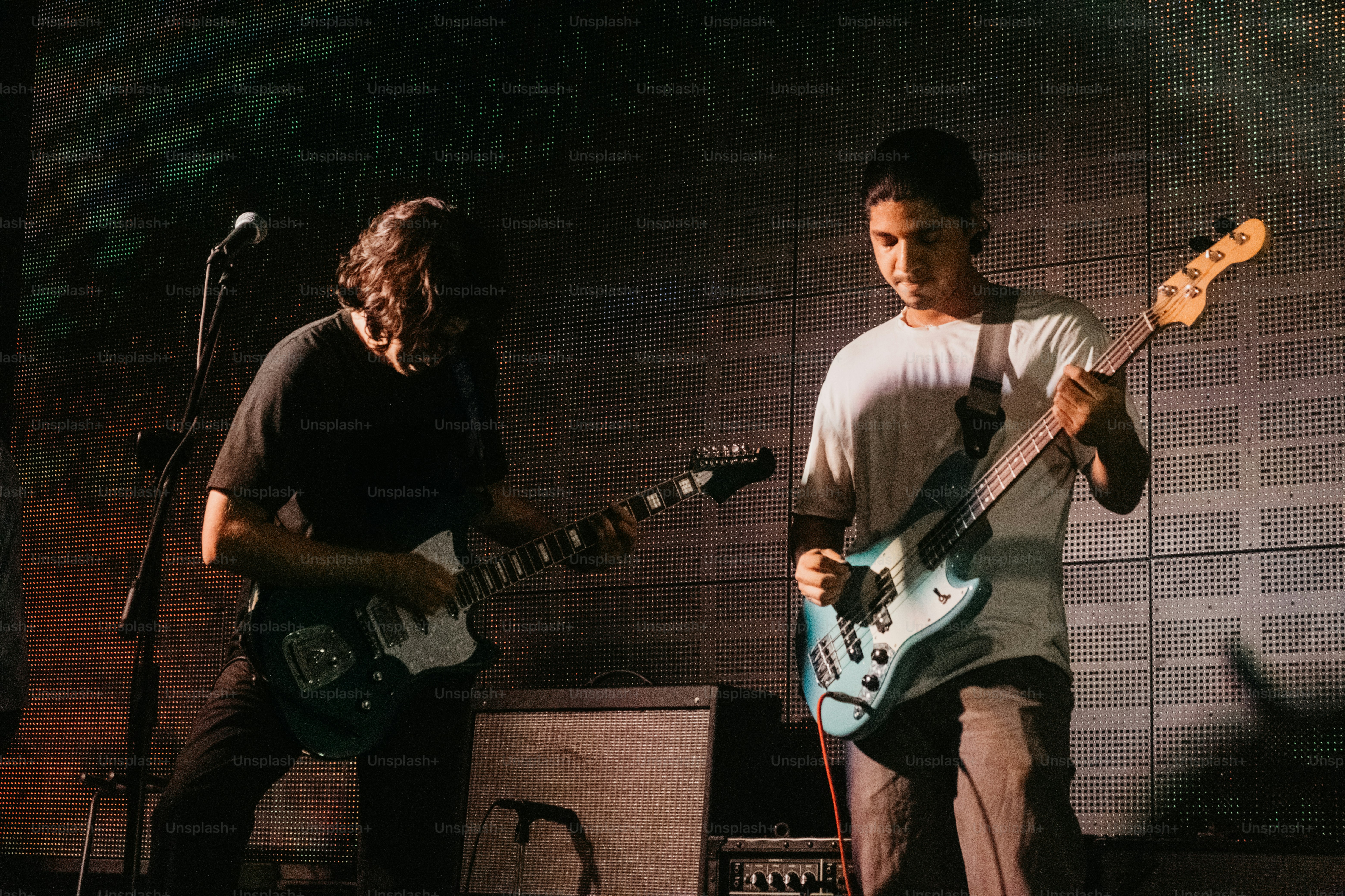 Two musicians playing electric guitar and bass on a stage with a grid background