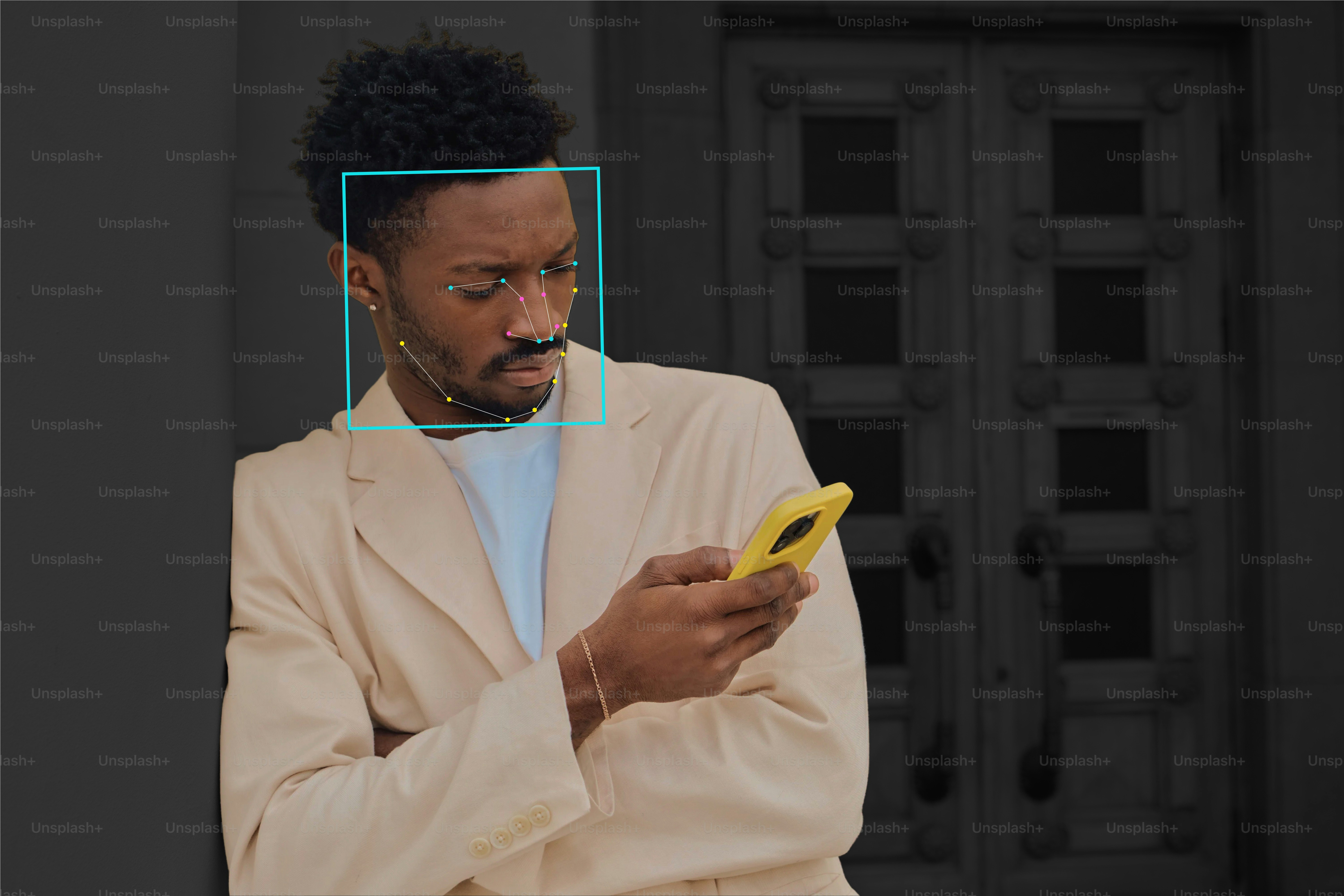 A man in a beige blazer looking at a yellow smartphone with facial recognition overlay