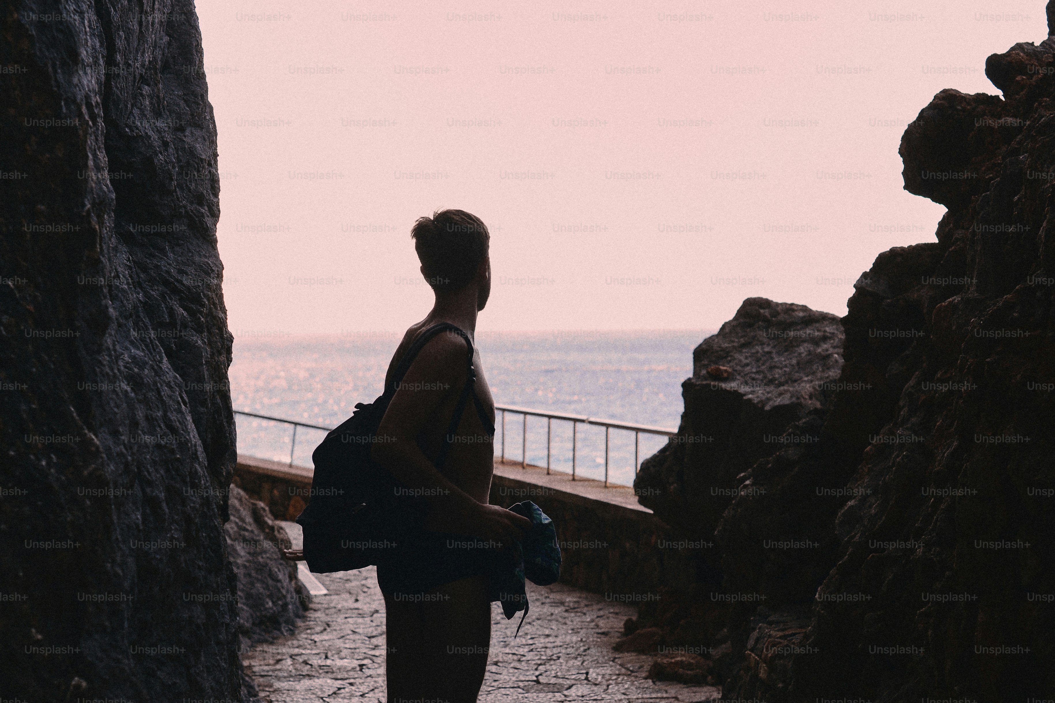 Une personne avec un sac à dos regardant vers la mer entre deux falaises rocheuses