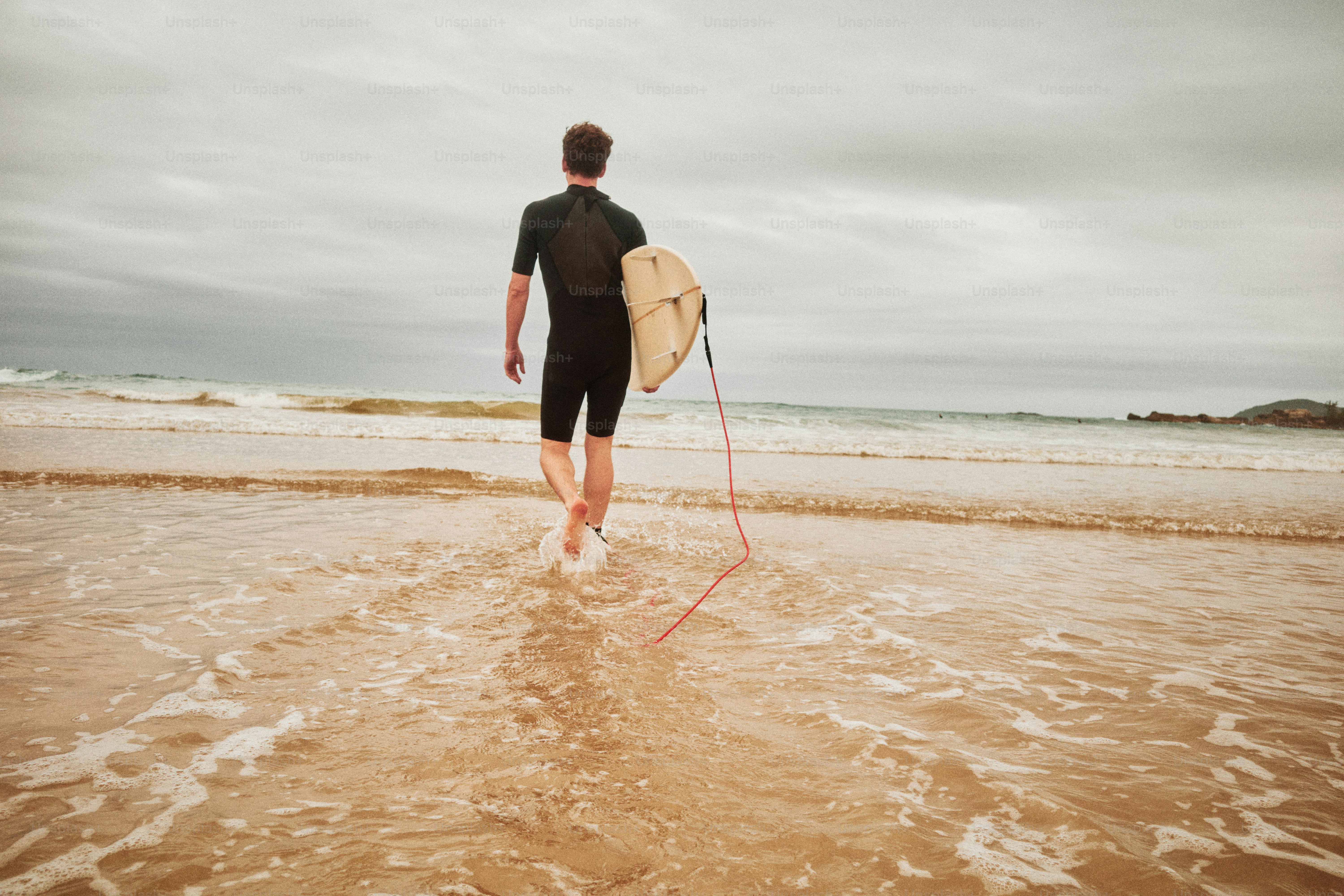 Une personne en combinaison plongée marchant dans l’océan en portant une planche de surf