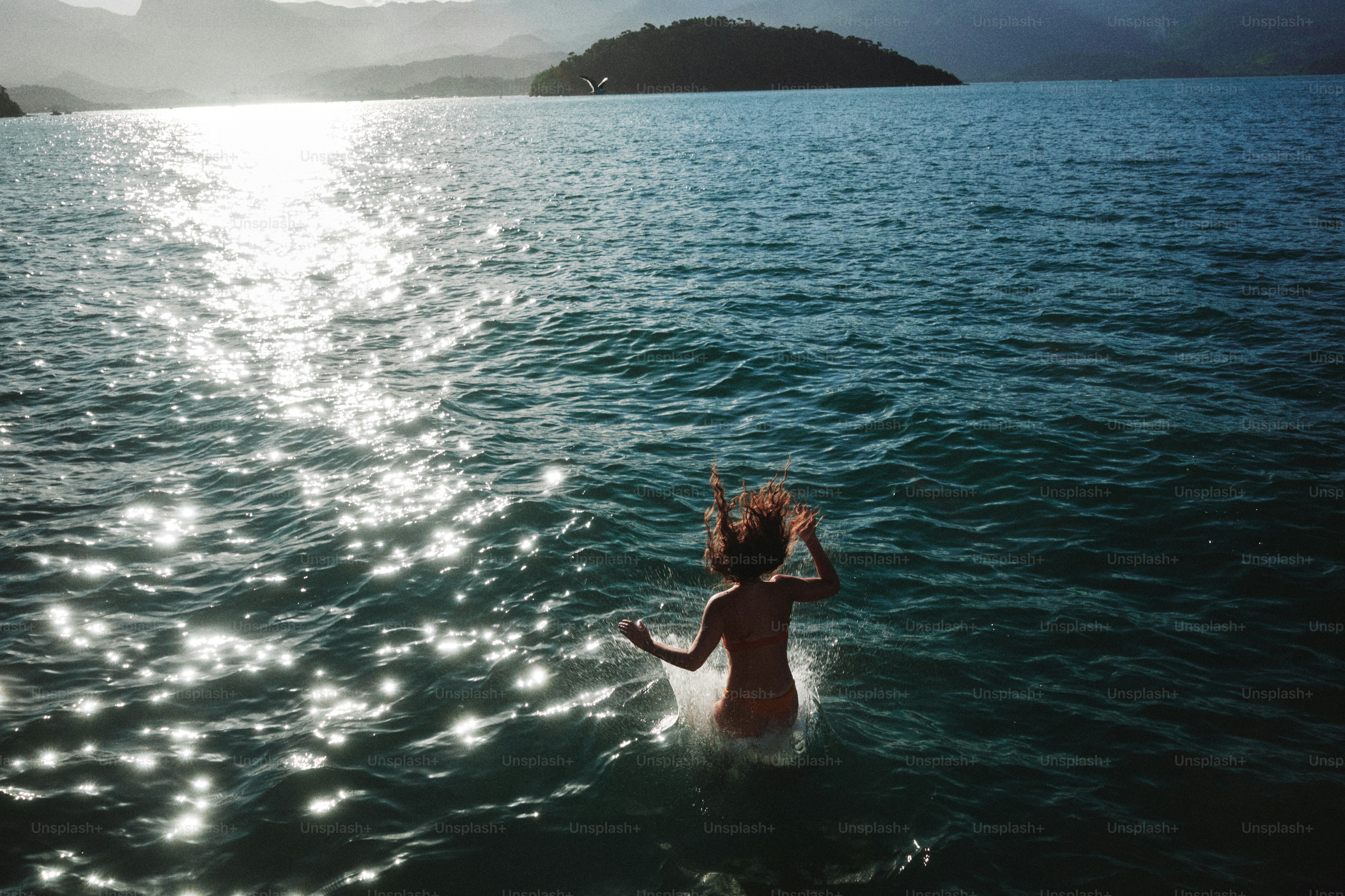 Une personne sautant dans une eau bleue scintillante avec une île lointaine en vue