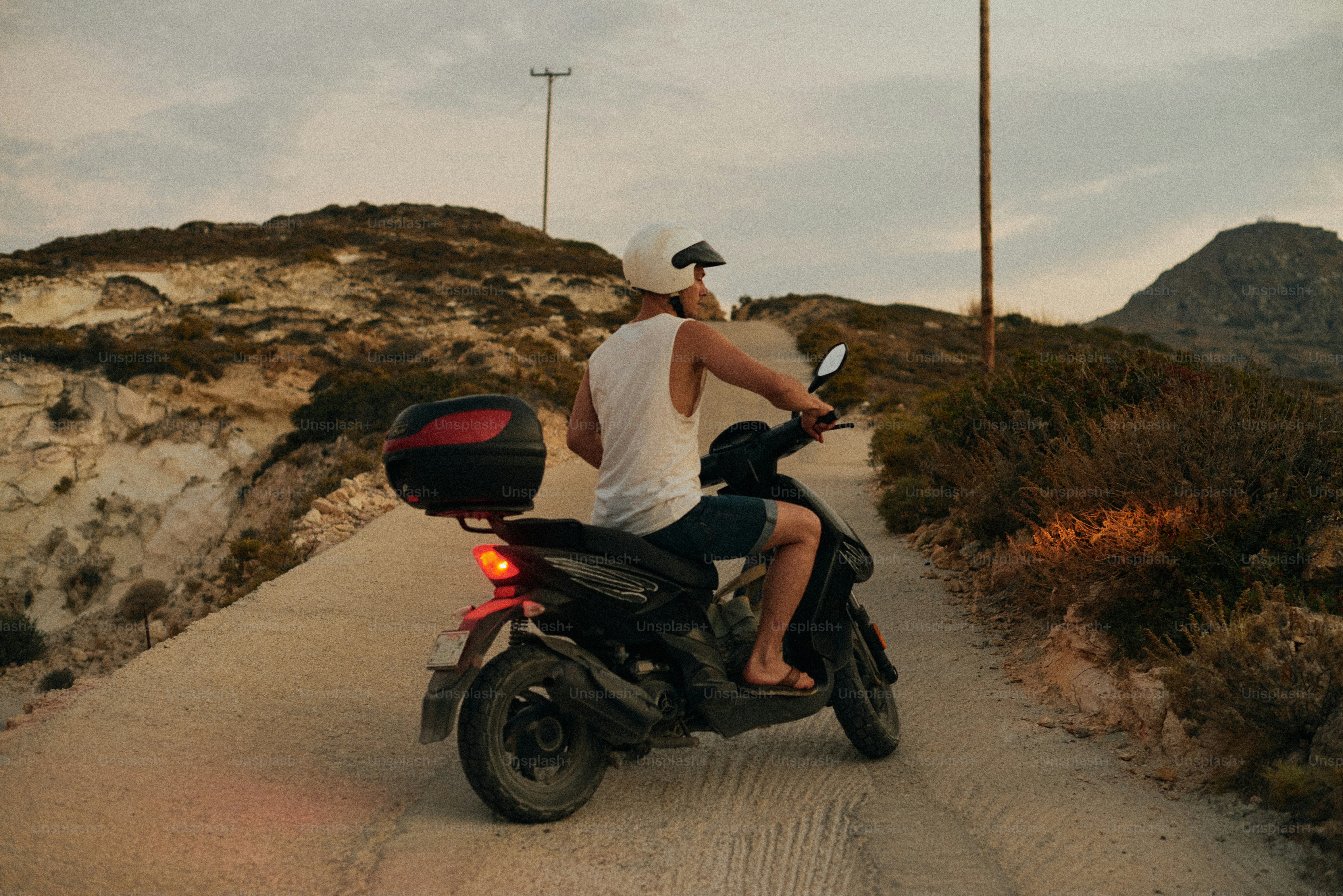 Une personne portant un casque blanc roulant en scooter sur un chemin de terre