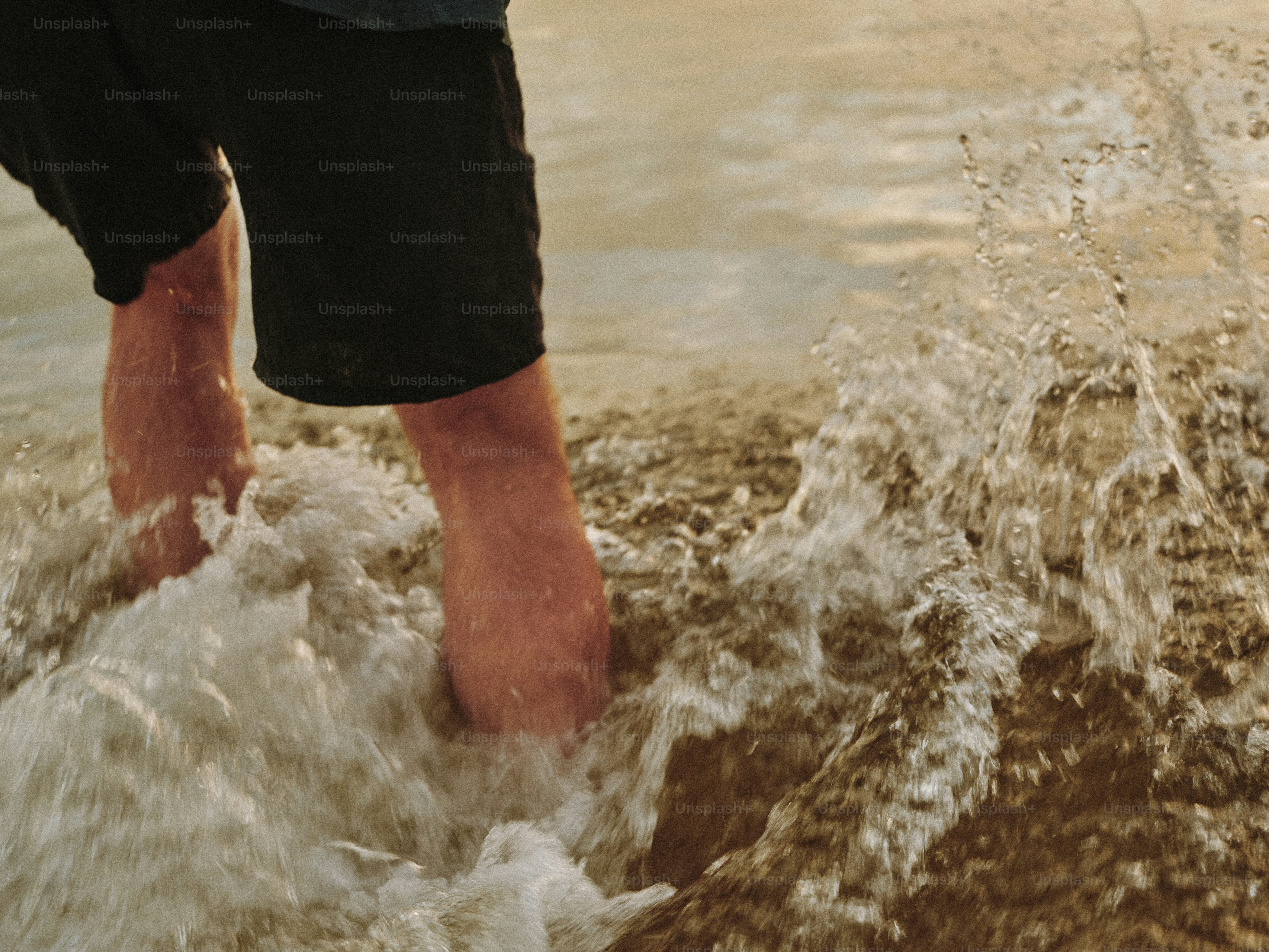 Une personne en short noir pataugeant dans l’eau éclaboussante sur la plage