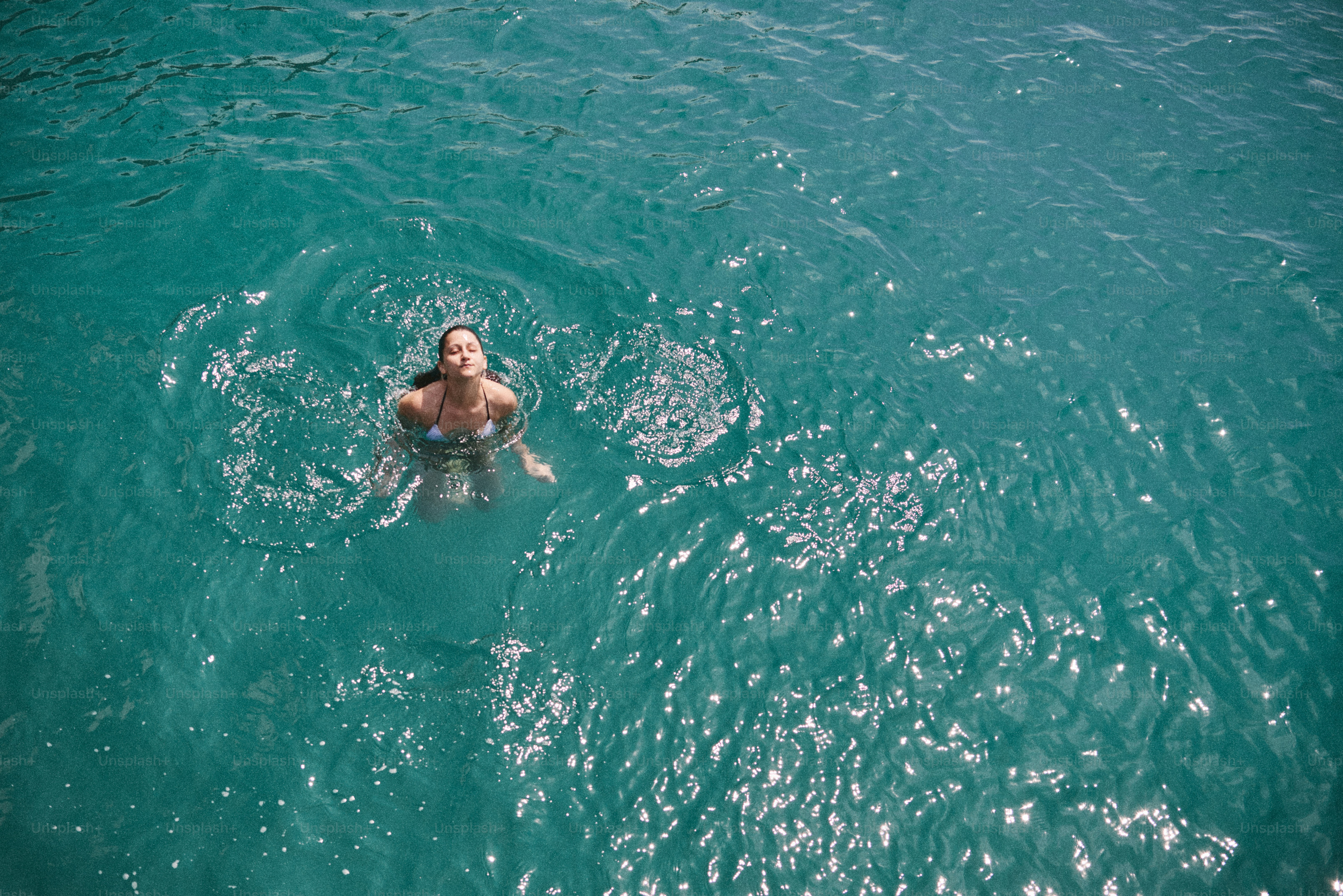 Une femme en bikini blanc nageant dans une eau turquoise claire