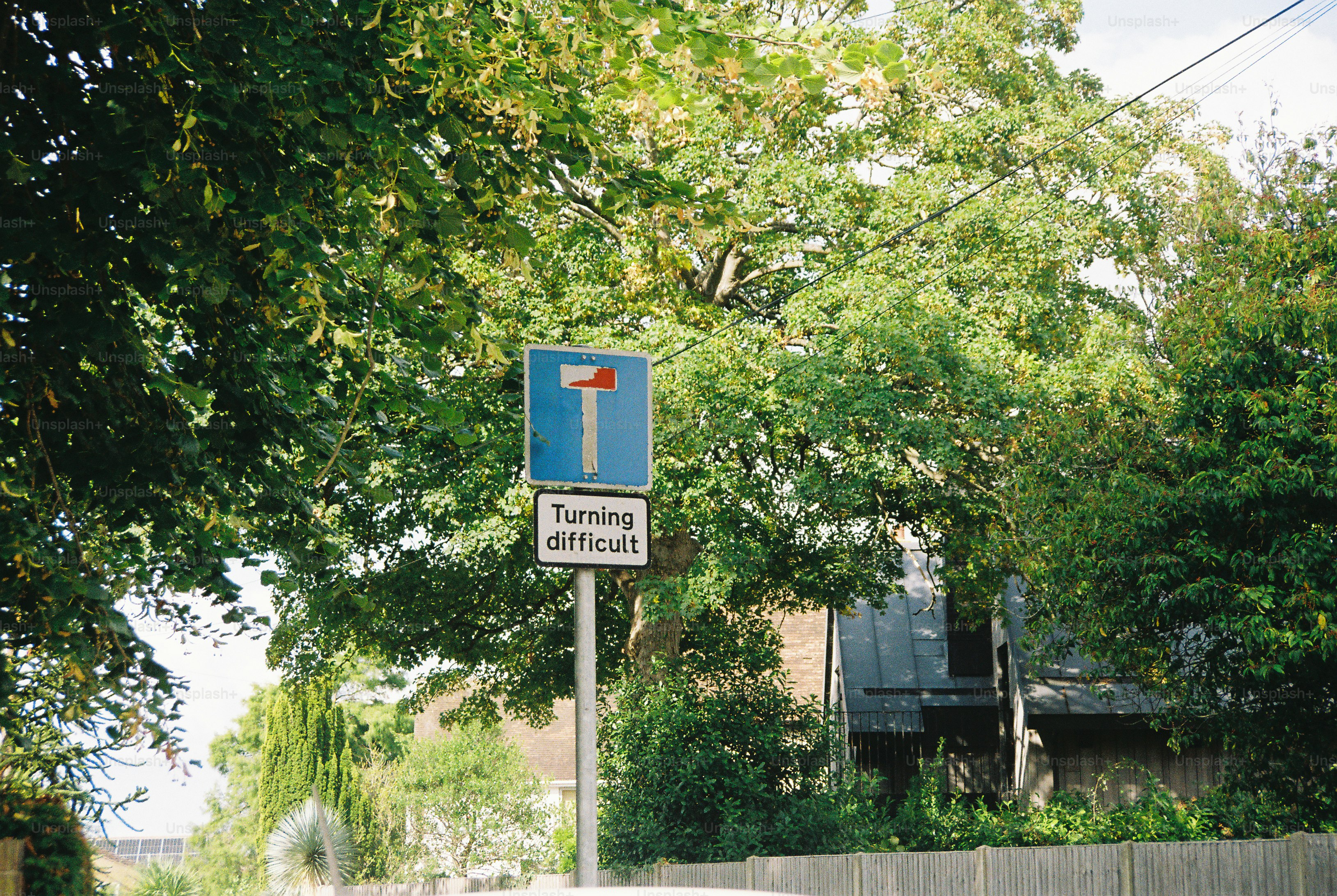 A blue road sign with a T-shaped symbol and a sign reading Turning difficult